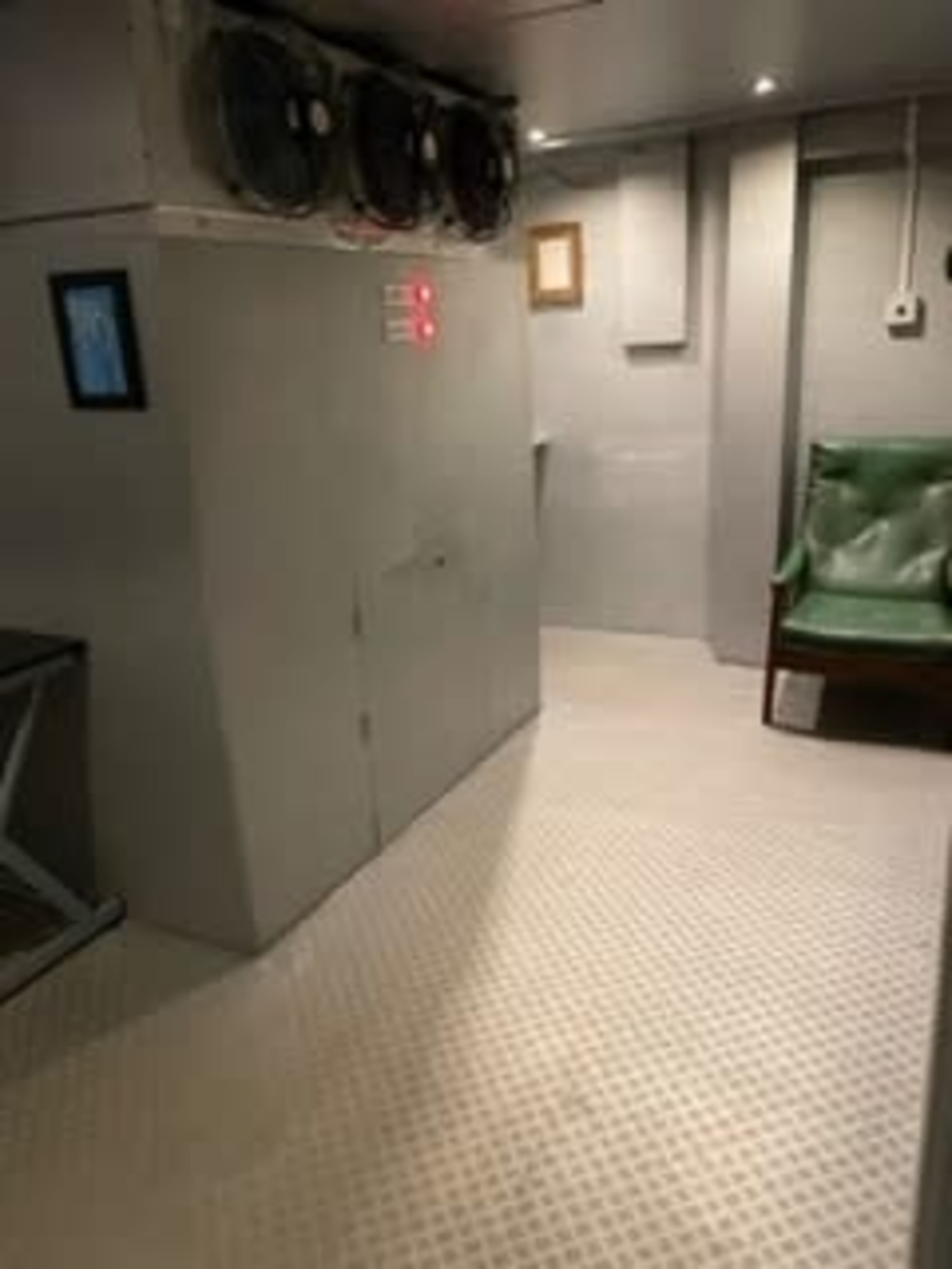 A gray interior space with air conditioning units mounted on the wall, a small control panel, and a green upholstered chair.