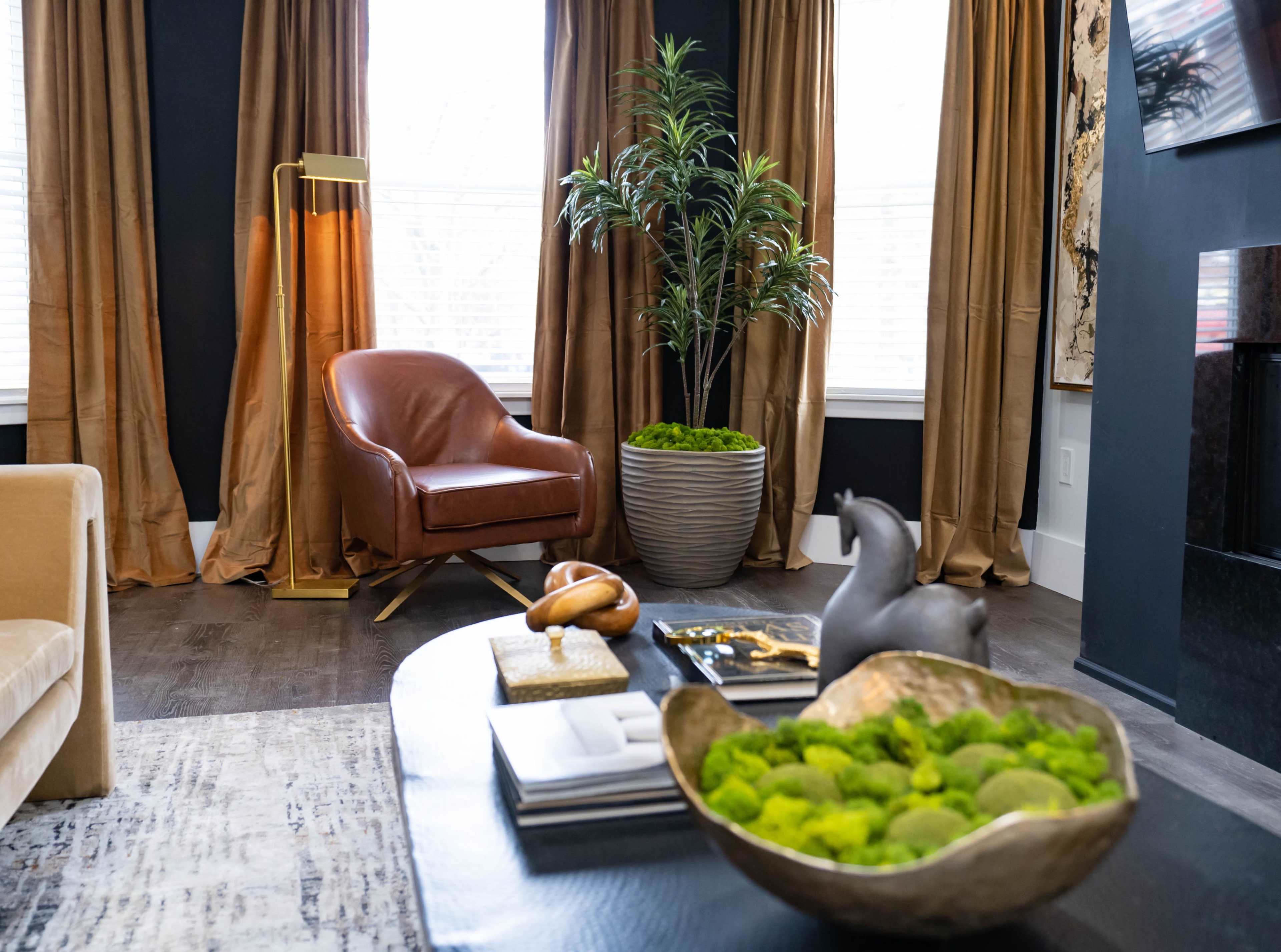 The image shows a cozy living room featuring a brown leather chair, a potted plant, and a coffee table adorned with decorative items and a bowl of green moss.