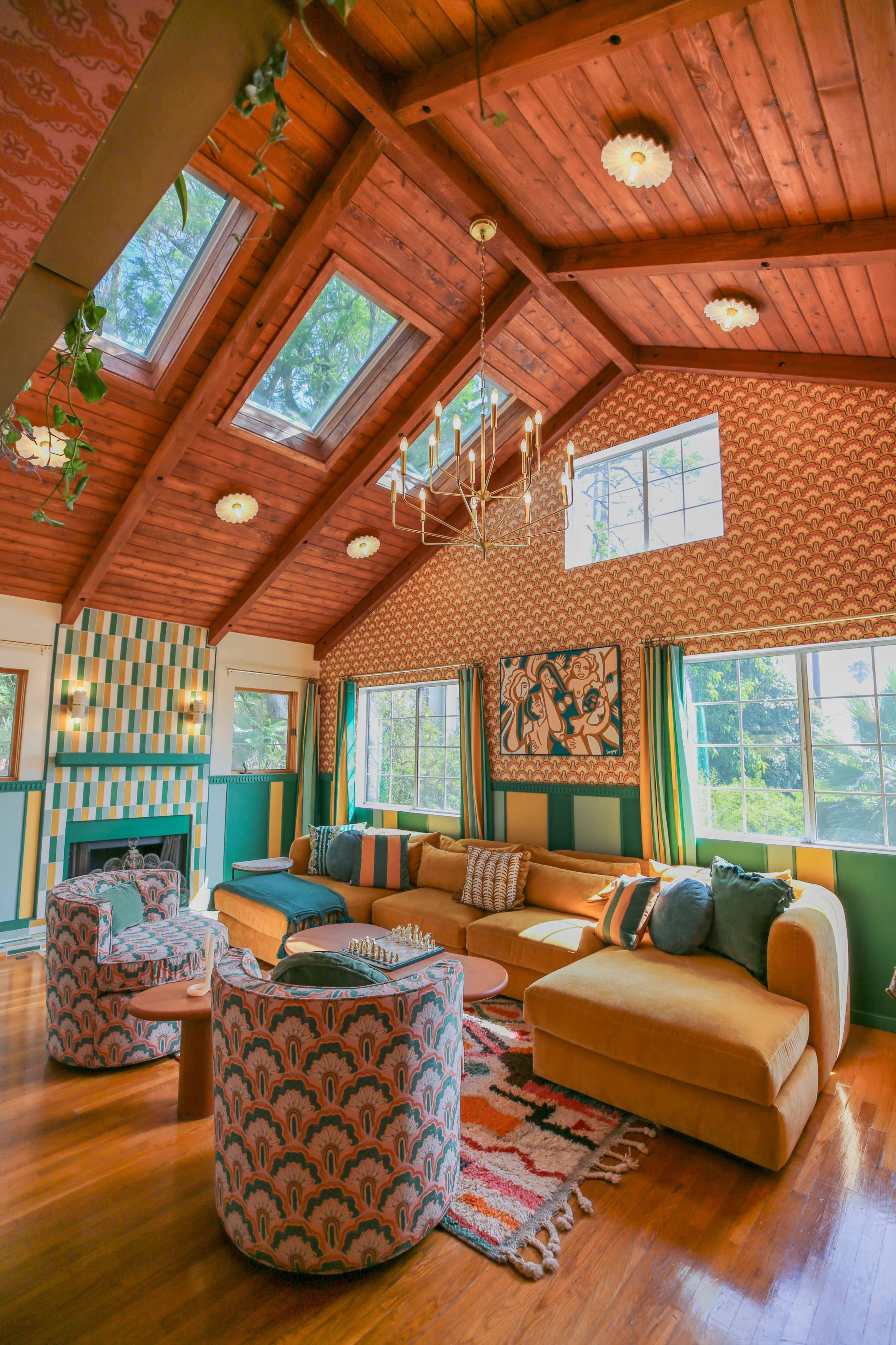 A spacious living room features a vaulted wooden ceiling, large windows, and a mix of colorful furnishings and patterns.