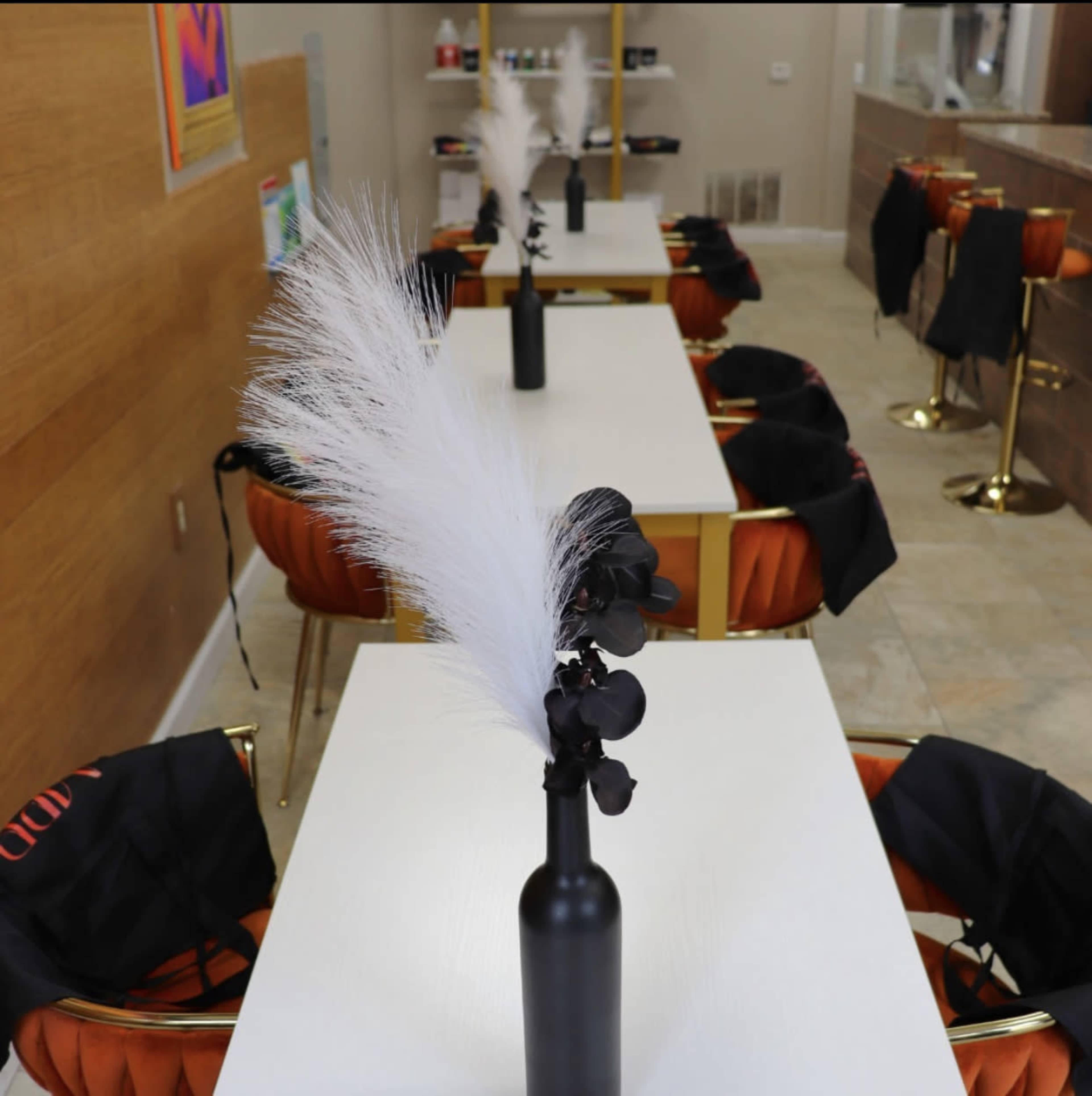 A modern interior with multiple tables set for a gathering, each featuring a tall decorative arrangement in a black bottle.