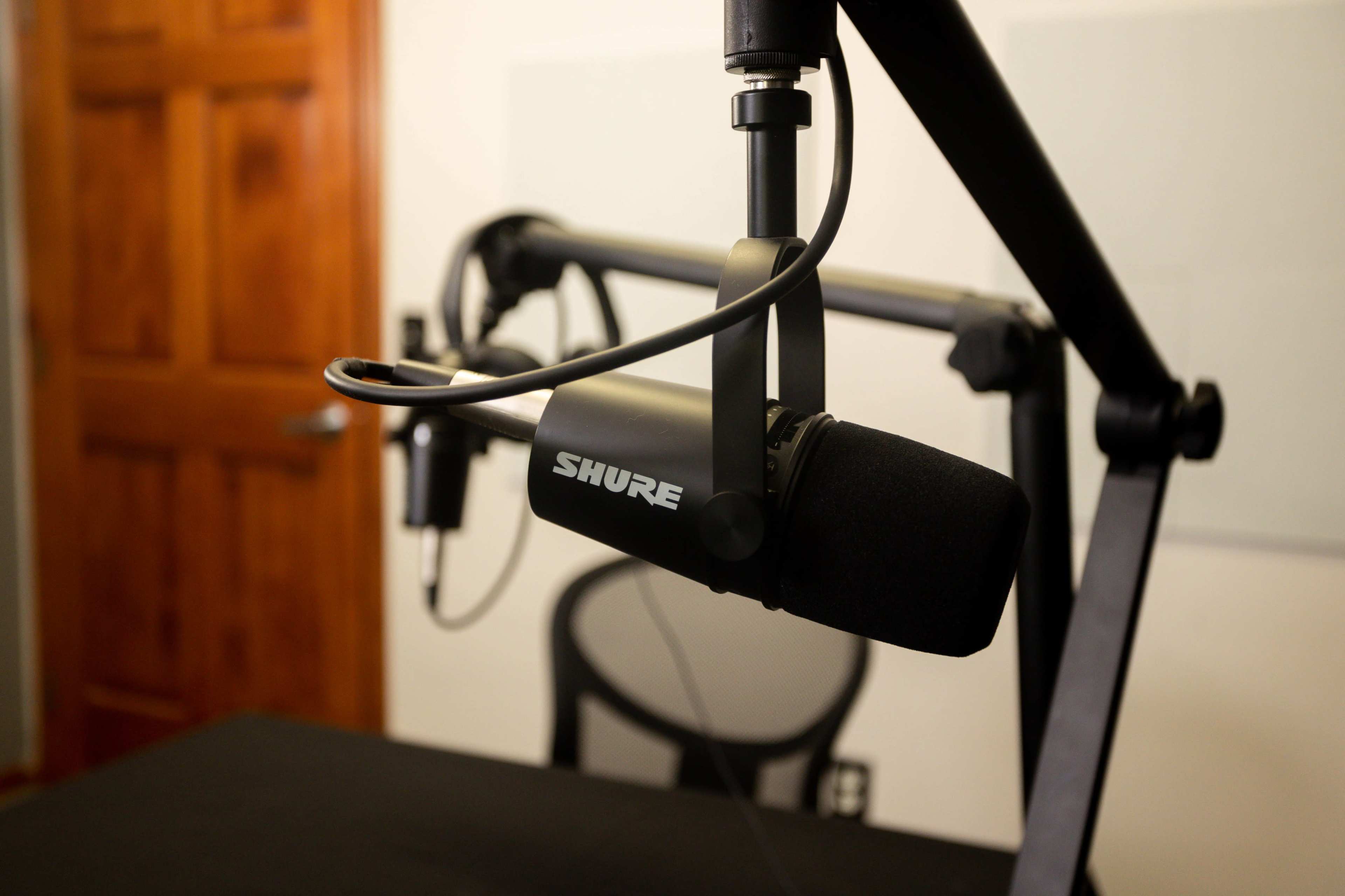 A Shure microphone is mounted on an adjustable arm above a black table in a recording studio.
