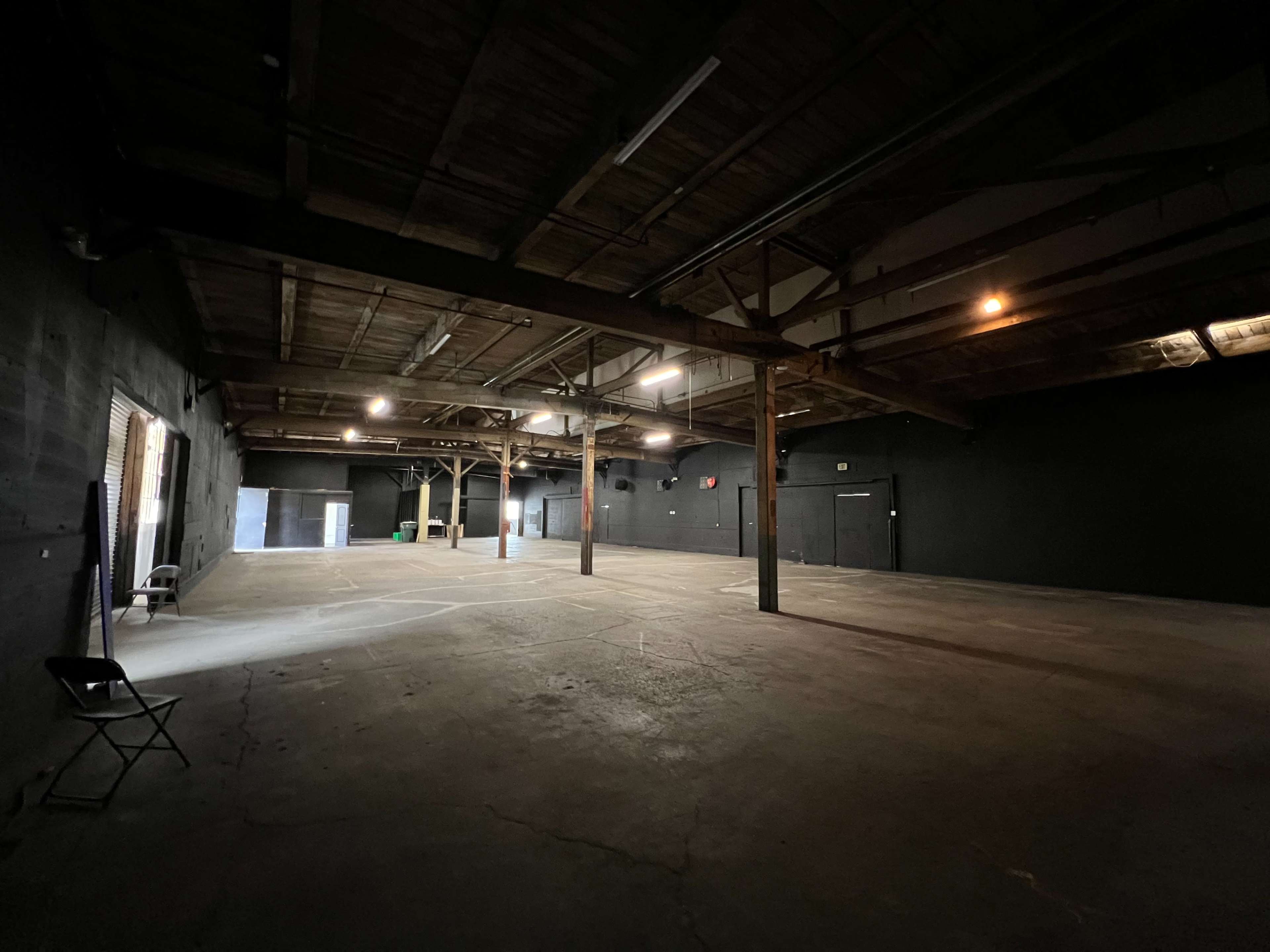 A spacious, empty industrial warehouse with exposed wooden beams and concrete floors.