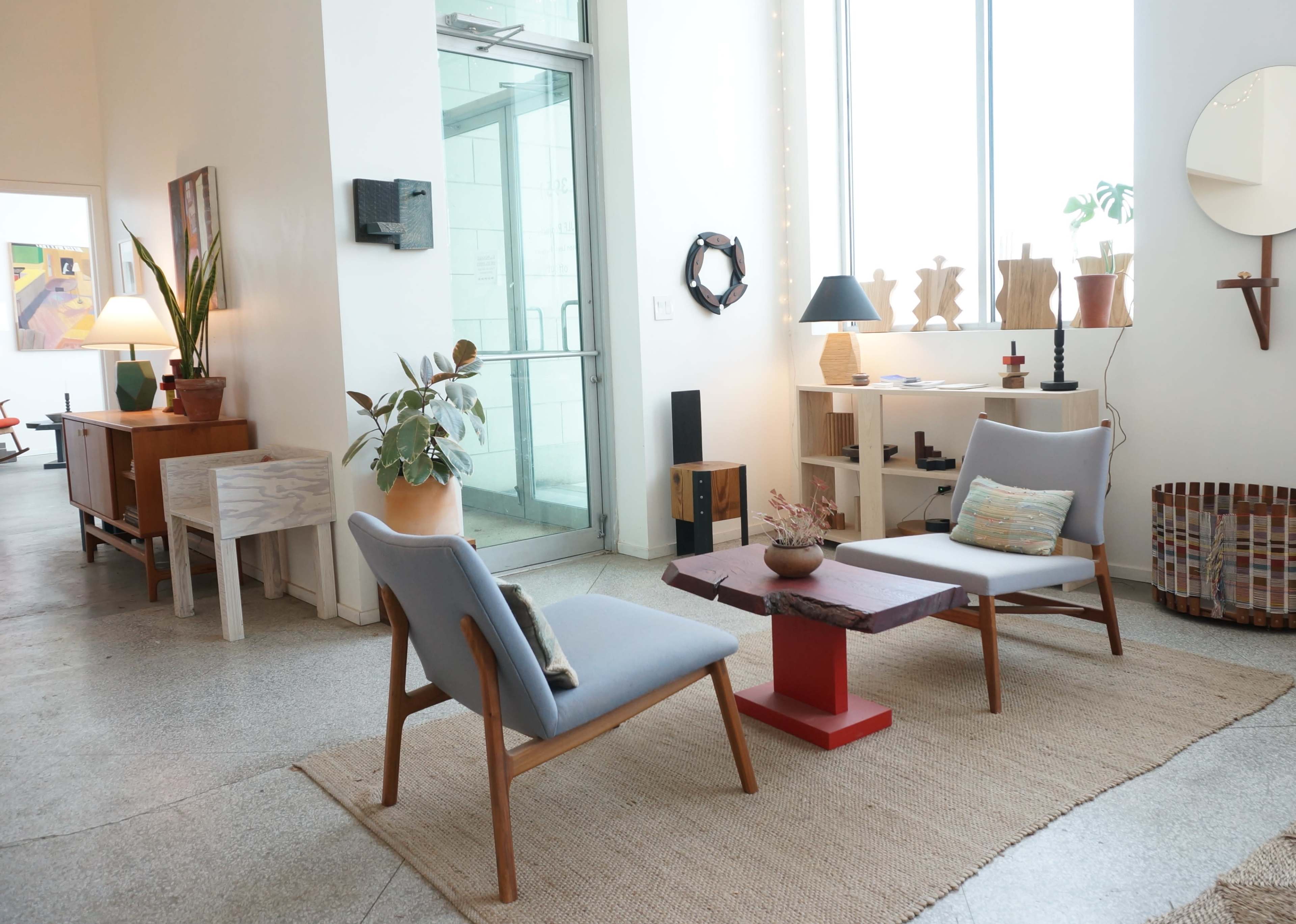 The image shows a spacious interior with two gray chairs facing a red and wooden coffee table, surrounded by various decorative objects and furniture.