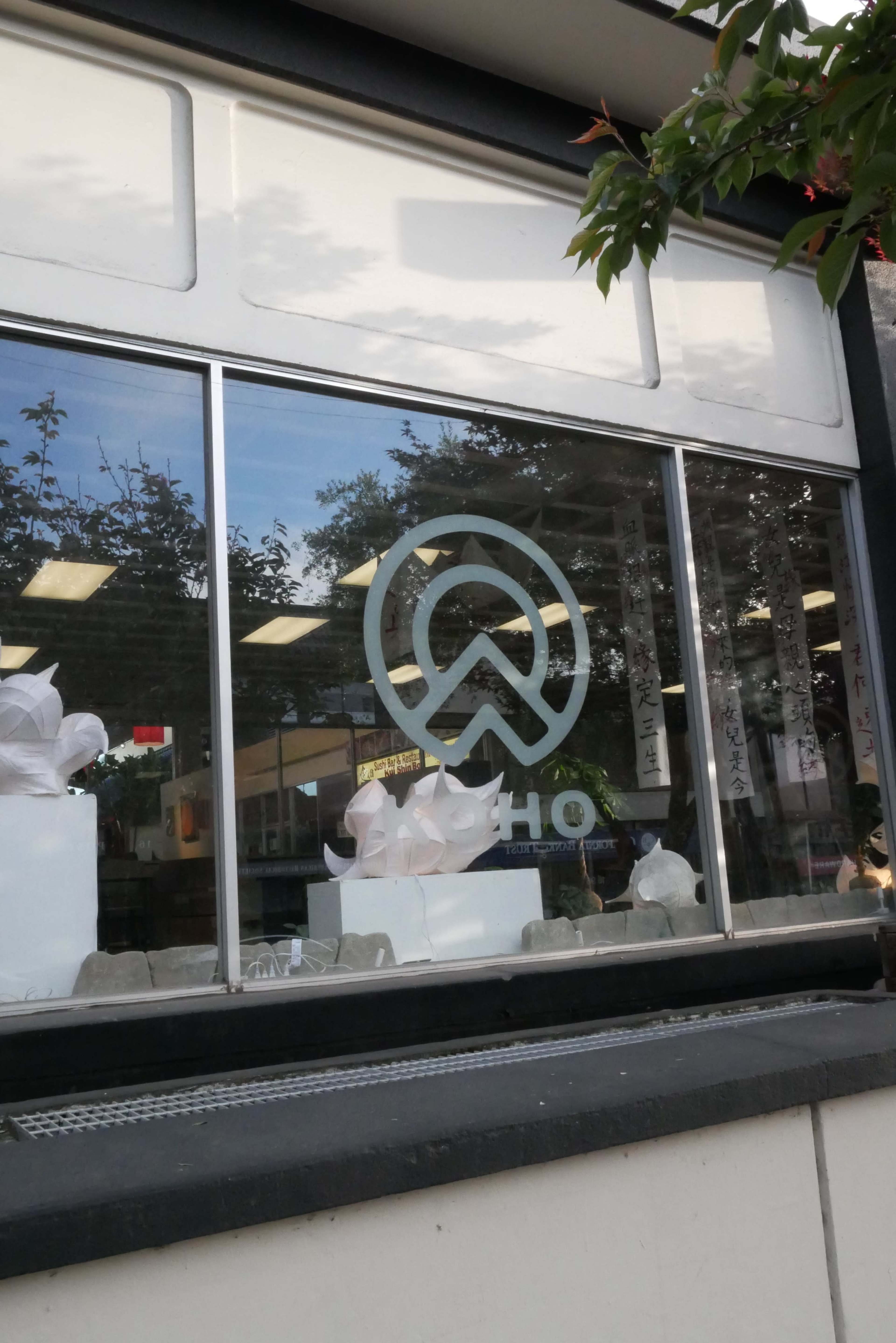 A large, stylized logo is displayed in the window of a shop, reflecting the outdoor scene.