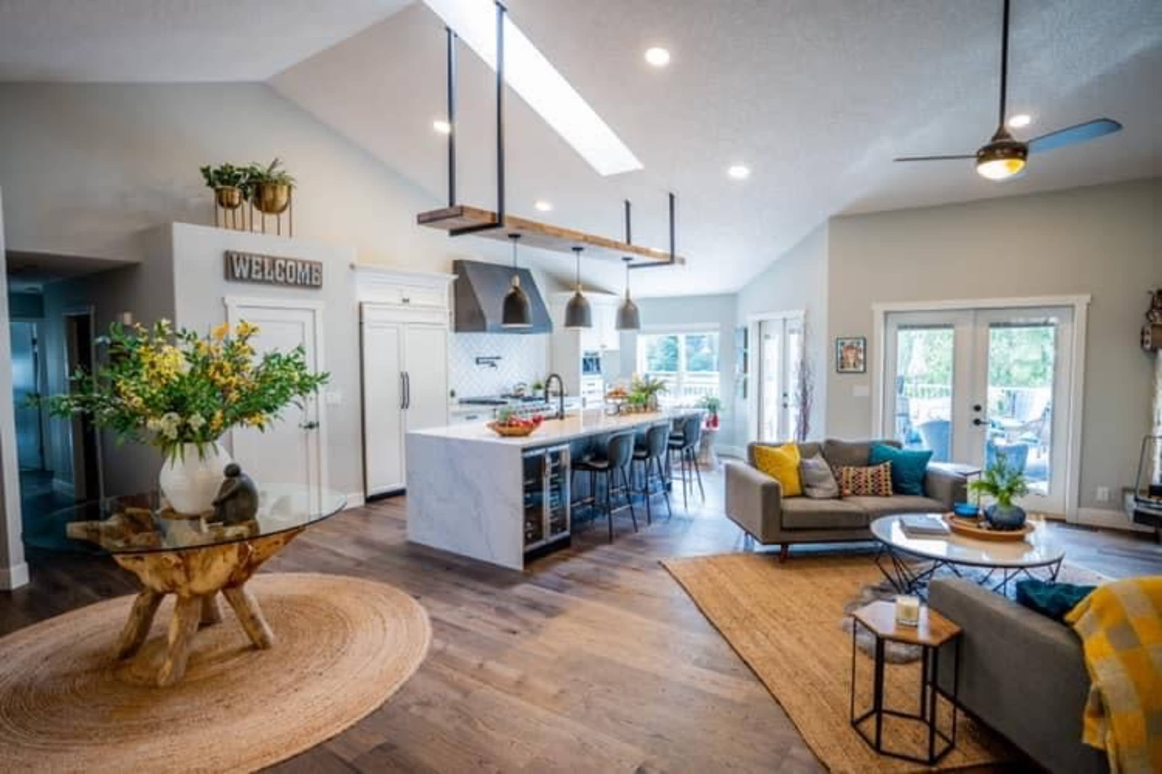A modern open-concept living space with a kitchen, dining area, and comfortable seating arrangements, featuring large windows and wooden flooring.