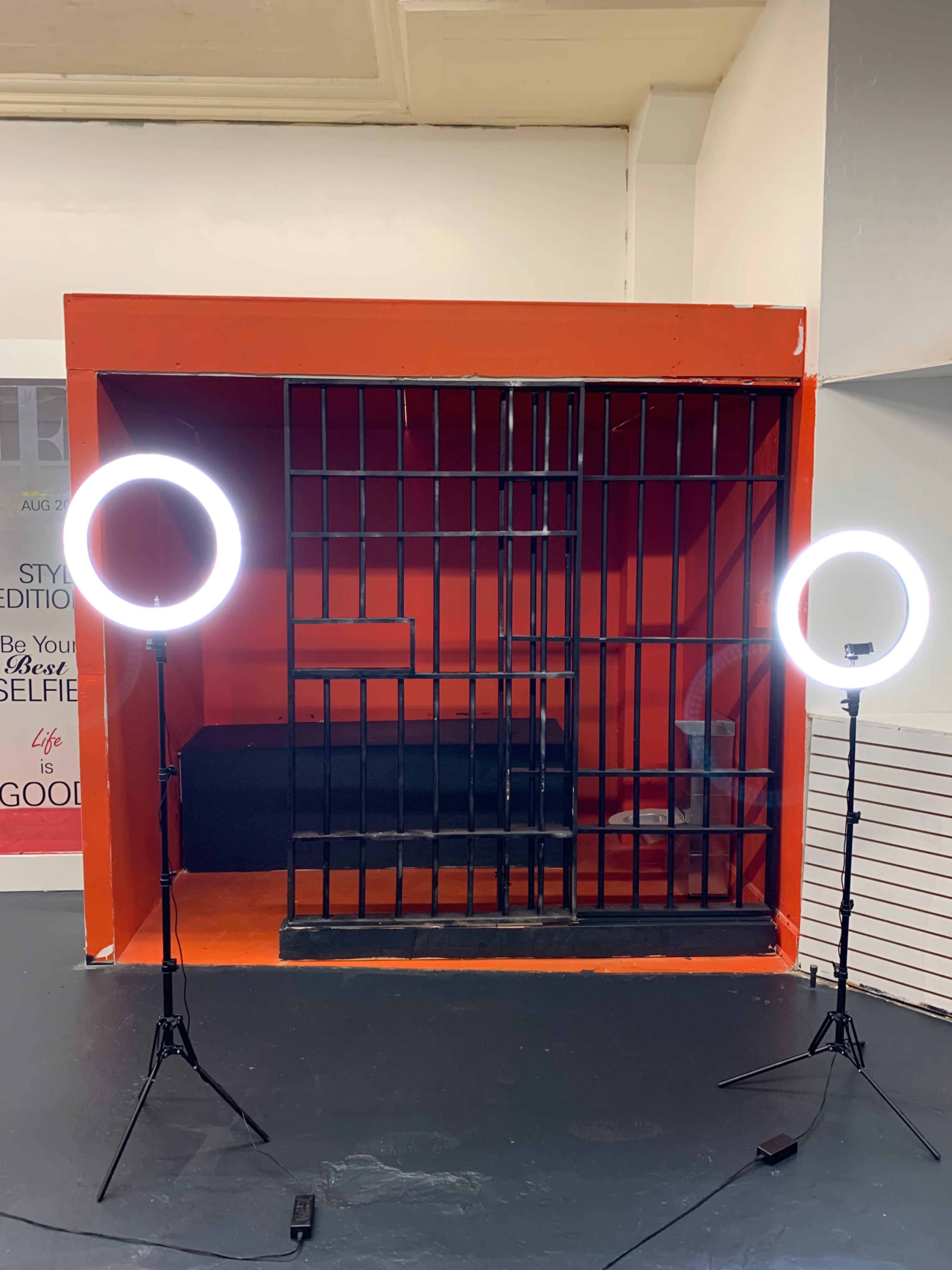 A photo booth set up with a bright orange background and two circular lighting rings positioned on either side of a black barred structure.