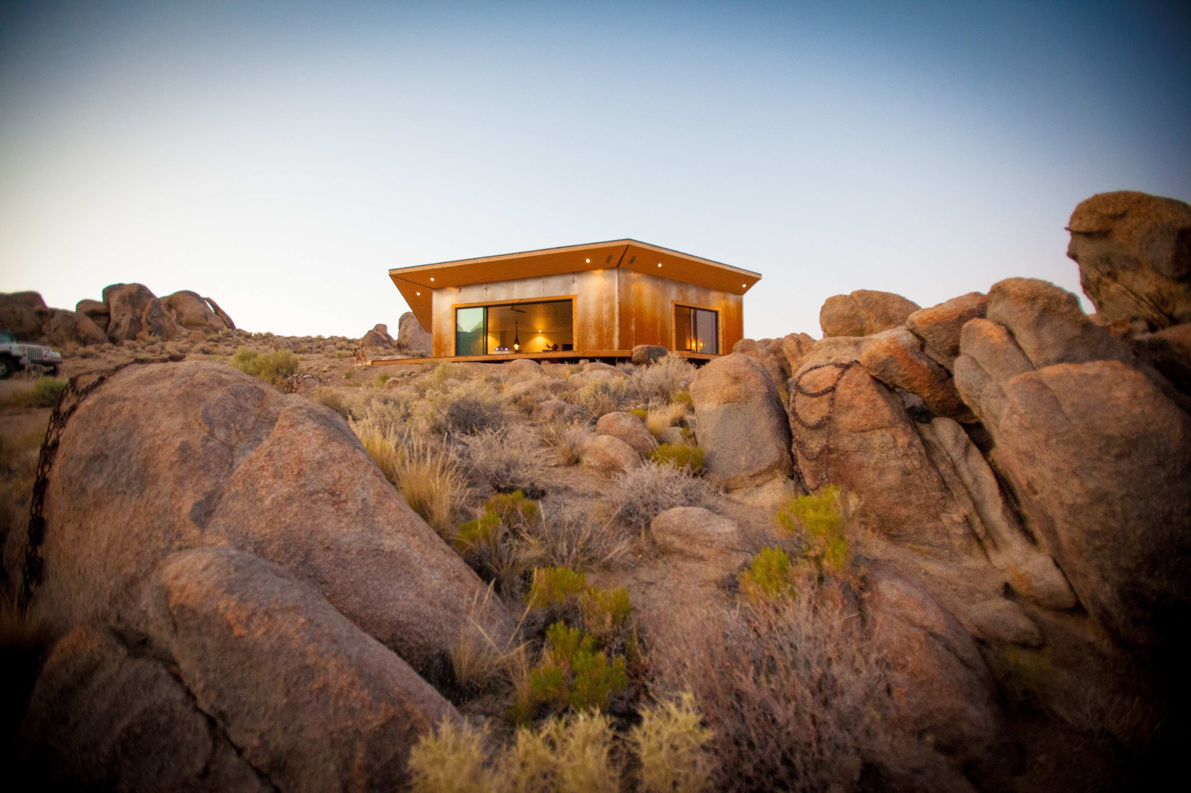 A modern house sits on a rocky hillside surrounded by sparse vegetation under a clear sky.