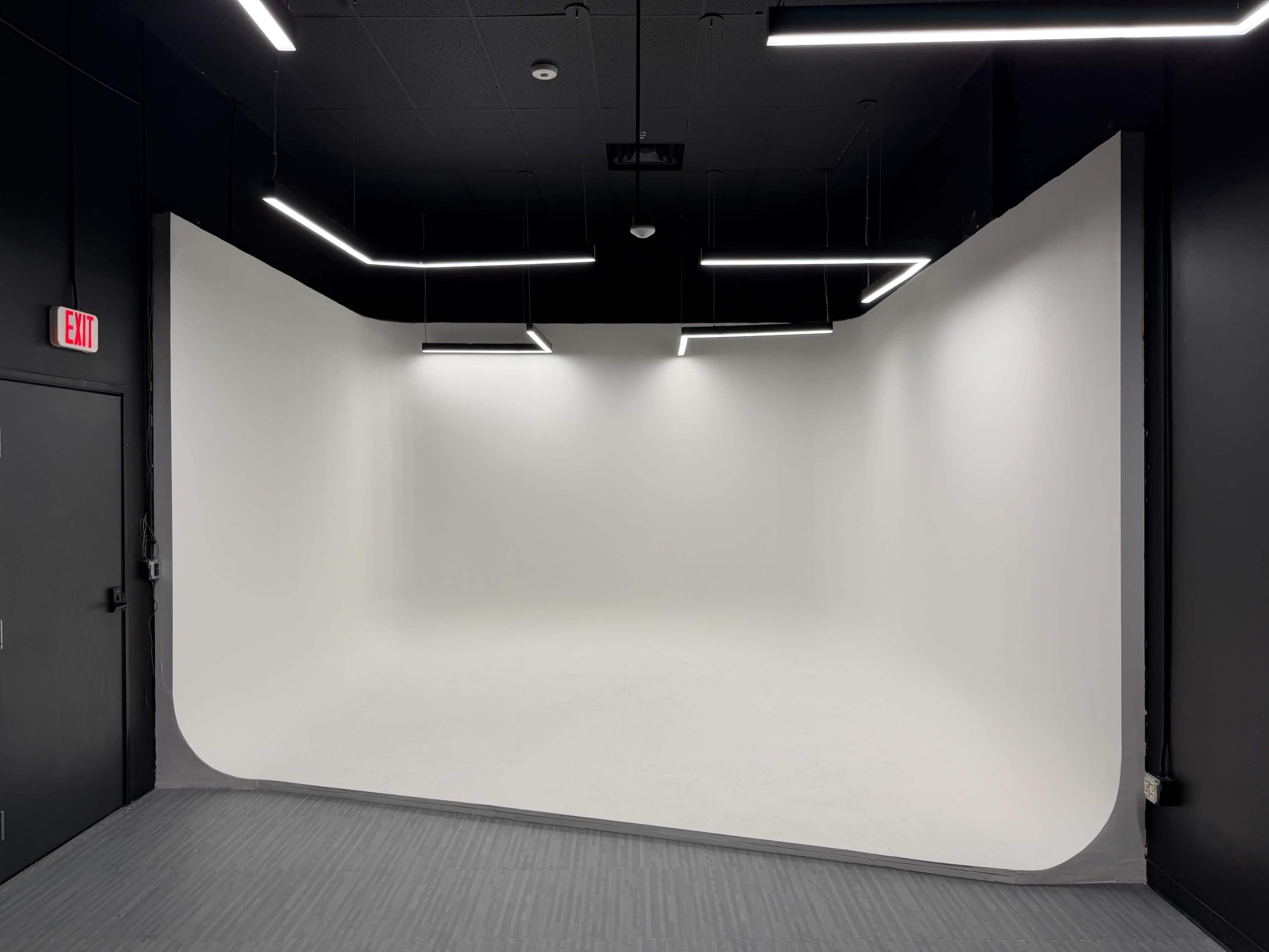 The image shows a spacious photo studio with a curved seamless backdrop, black walls, and modern lighting fixtures.