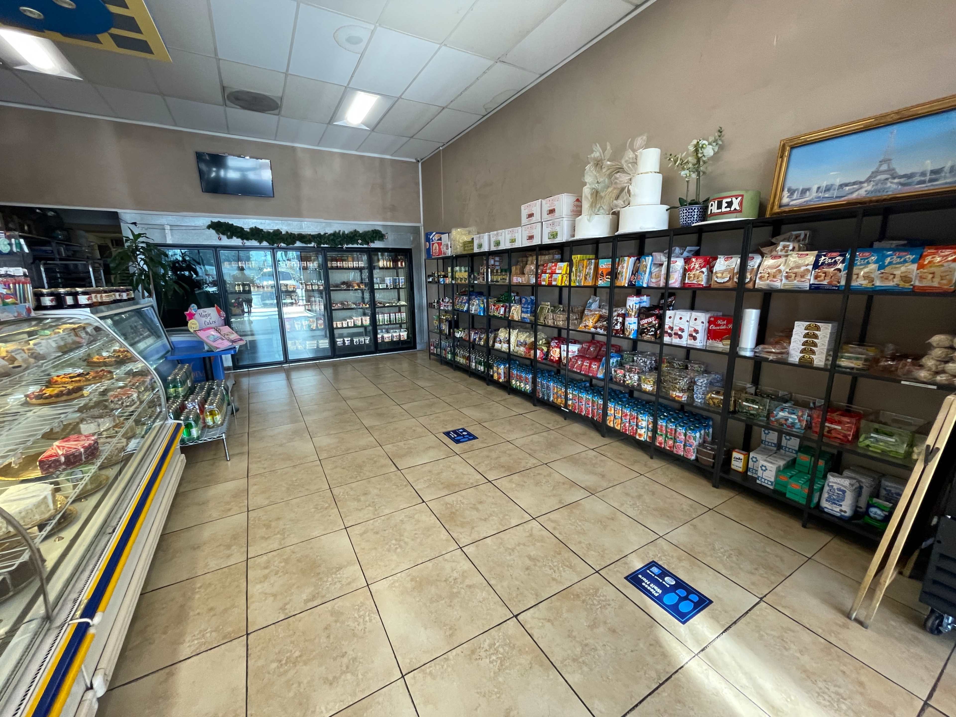 The image shows the interior of a small store featuring shelves filled with packaged snacks and beverages, a refrigerated display case, and a glass entrance.