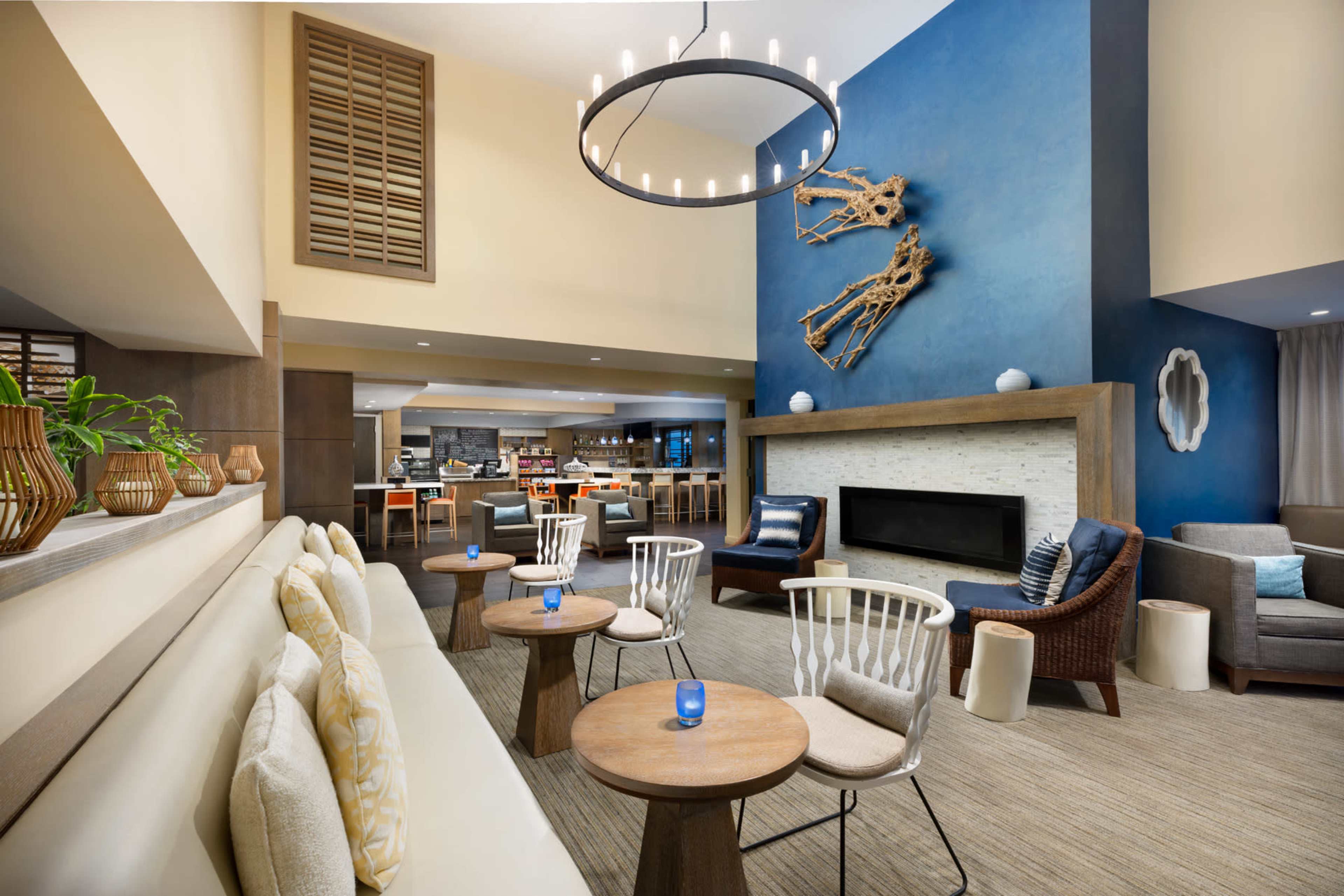 The image shows a modern lounge area with a mix of seating options, a fireplace, and a blue accent wall featuring decorative wooden art.