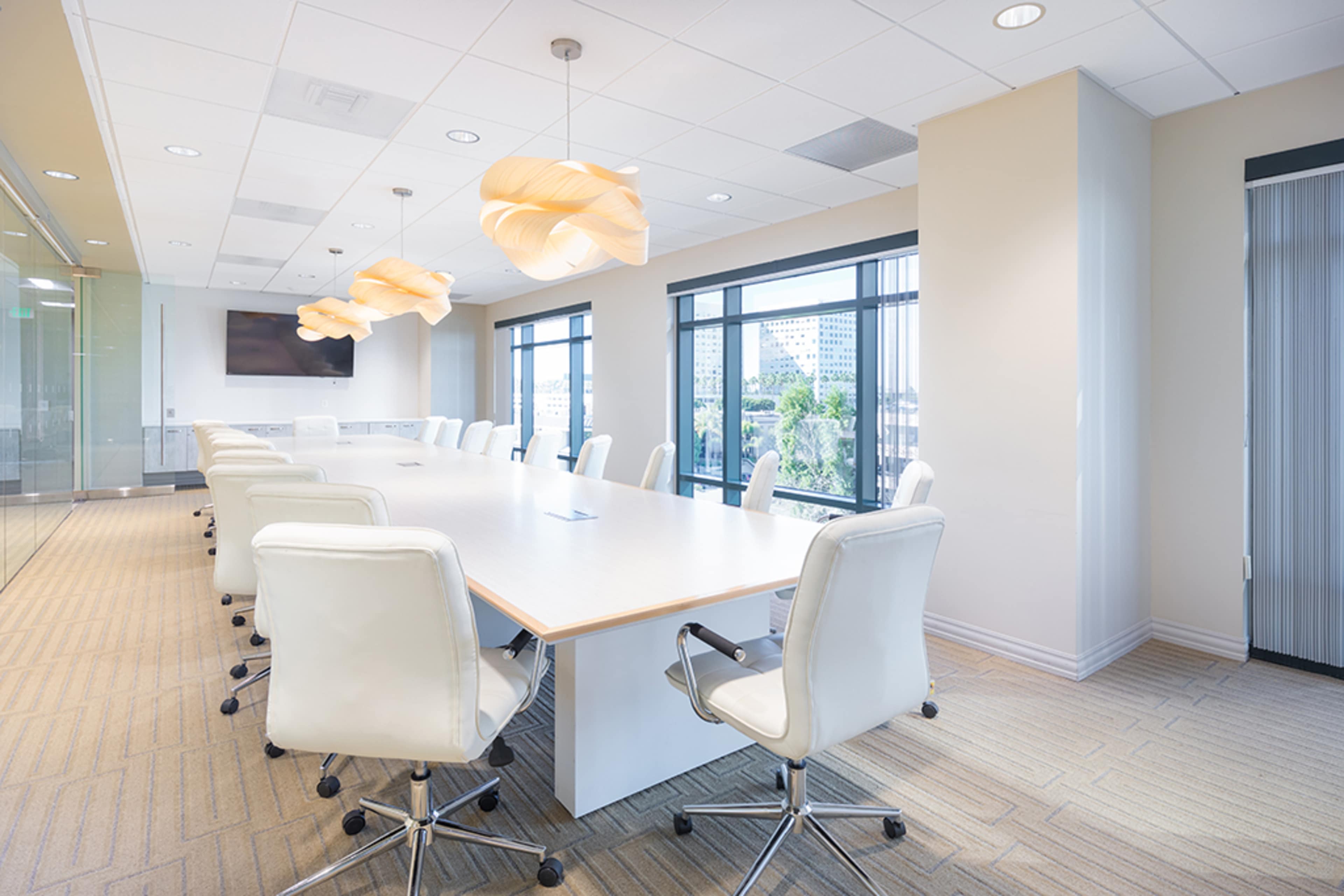 A large conference room features a long white table surrounded by modern swivel chairs and illuminated by unique pendant lights.