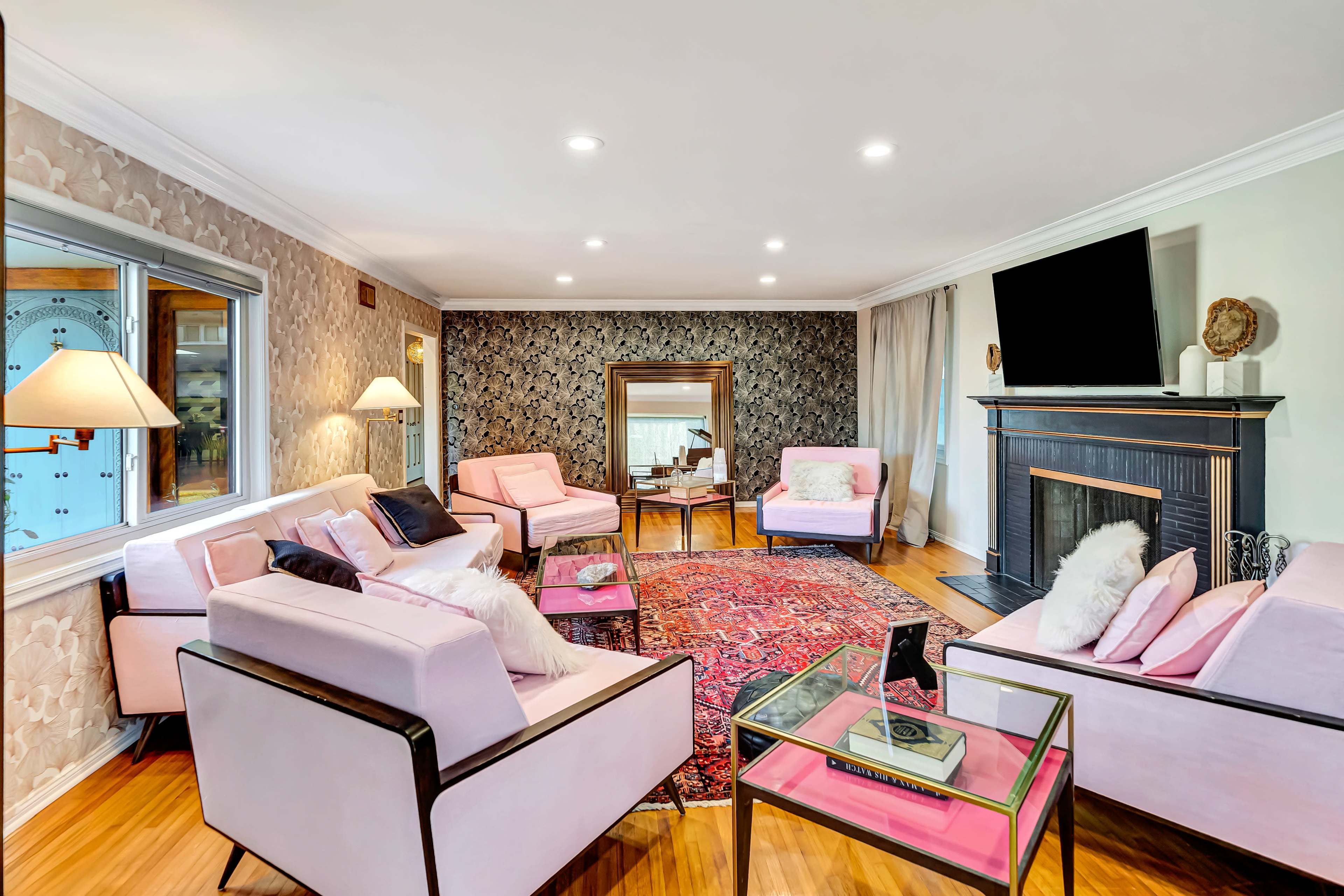 A spacious living room features pink upholstered sofas, a decorative rug, and a black fireplace with a large mirror on the wall.