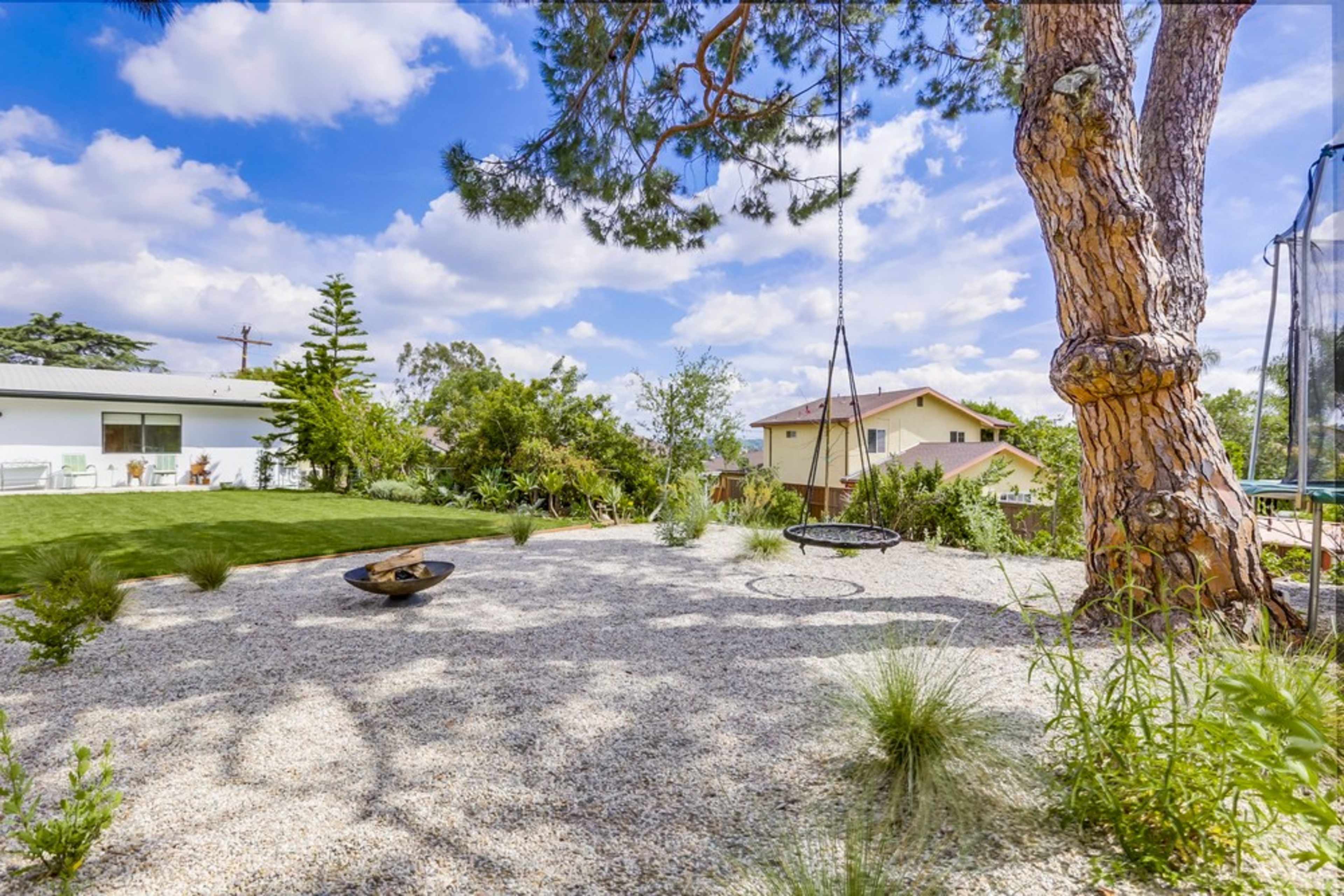A landscaped backyard with a swing hanging from a tree, gravel ground cover, and surrounding greenery.