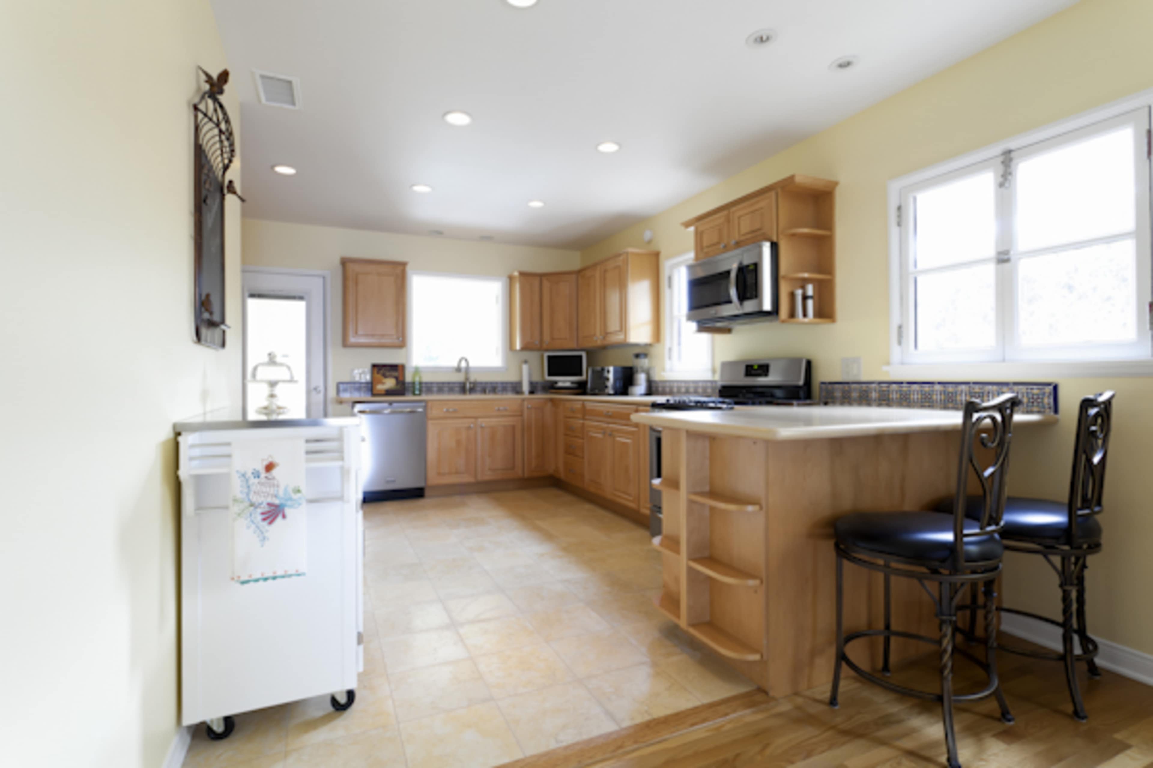 The image shows a kitchen with wooden cabinets, stainless steel appliances, and a small table with high-backed chairs.