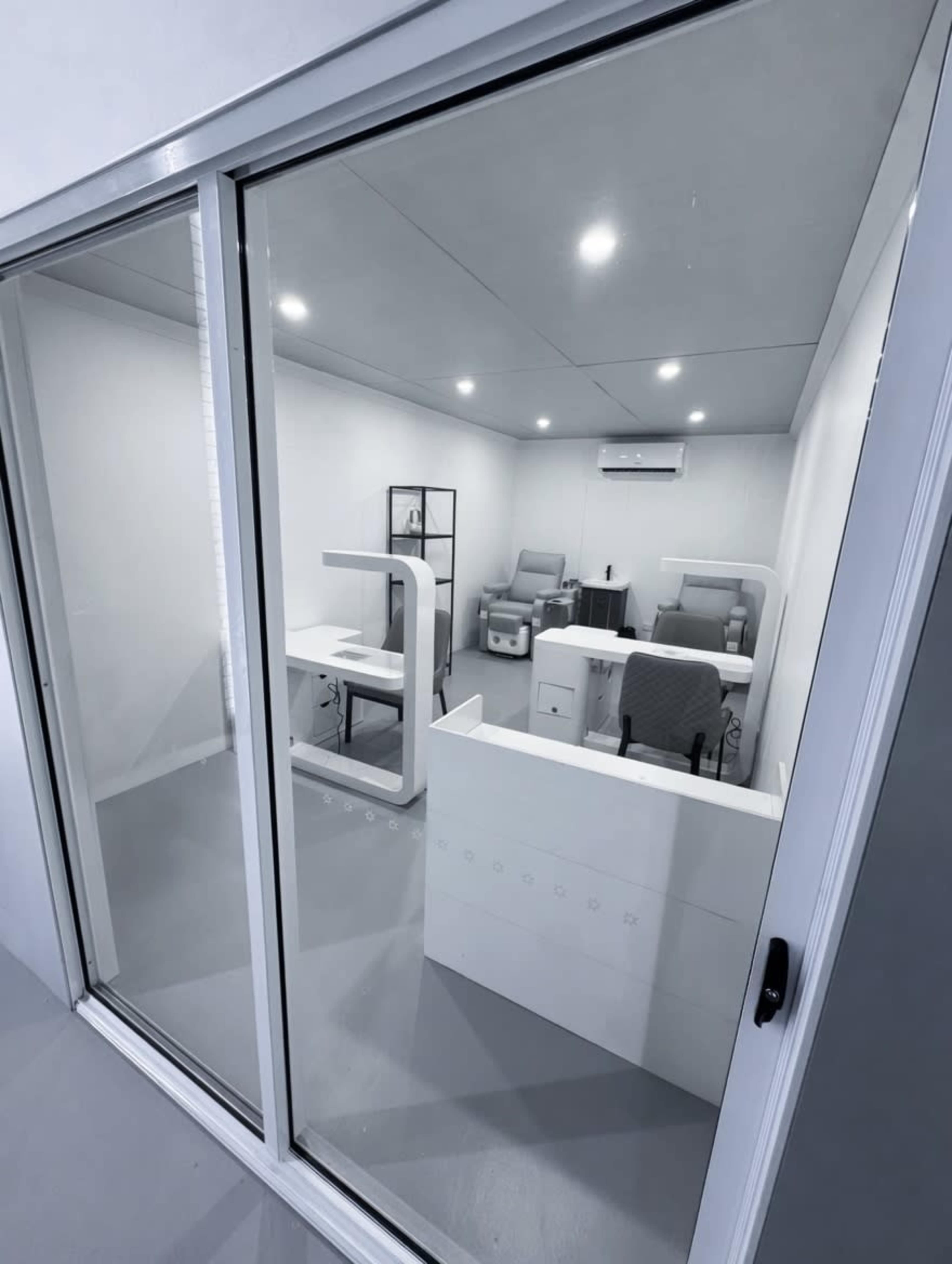 The image shows a bright, modern office space with multiple workstations, including desks and chairs, arranged inside a glass-enclosed room.