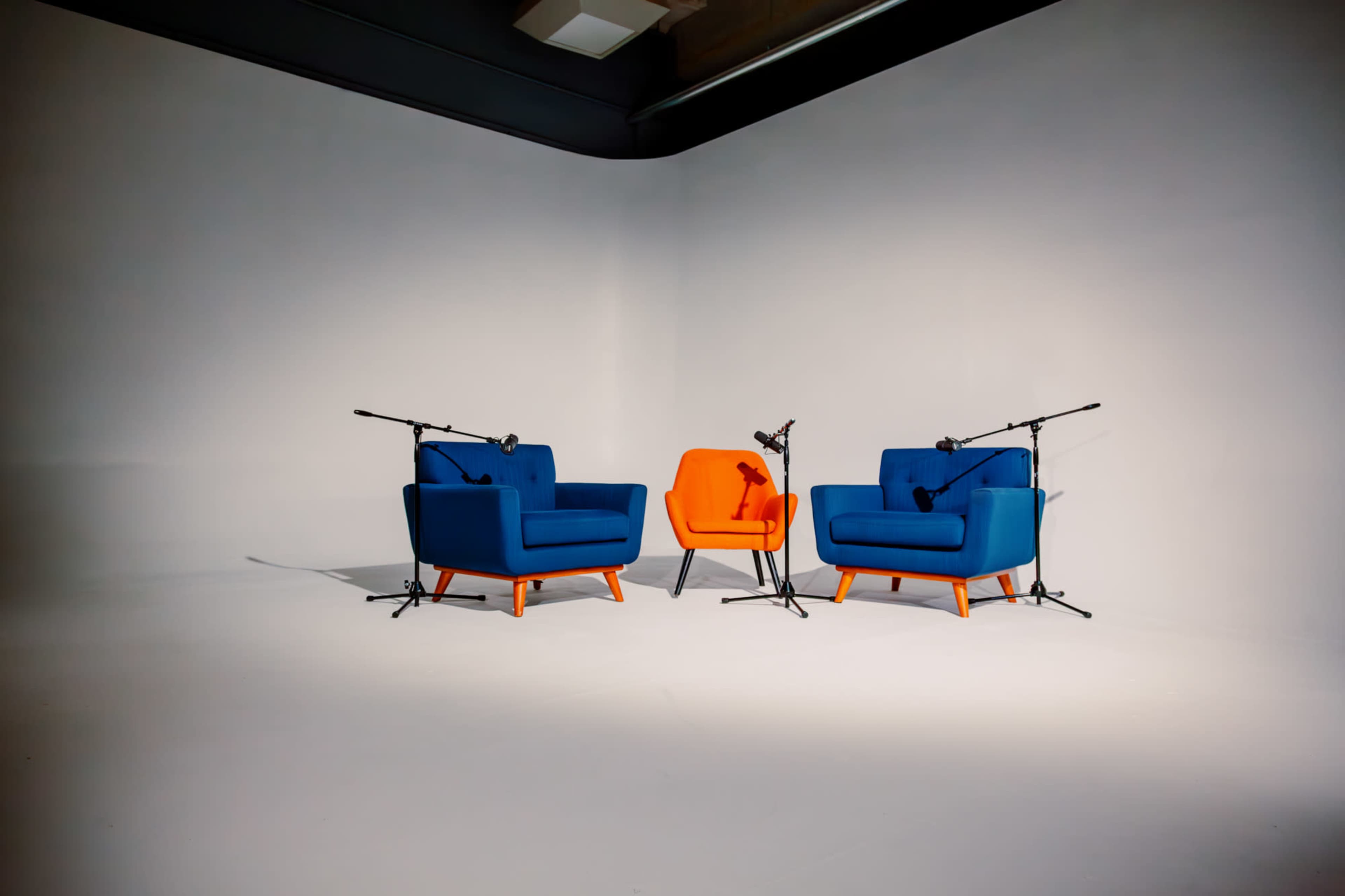 Two armchairs, one blue and one orange, positioned in a minimalist room with microphones mounted on stands.