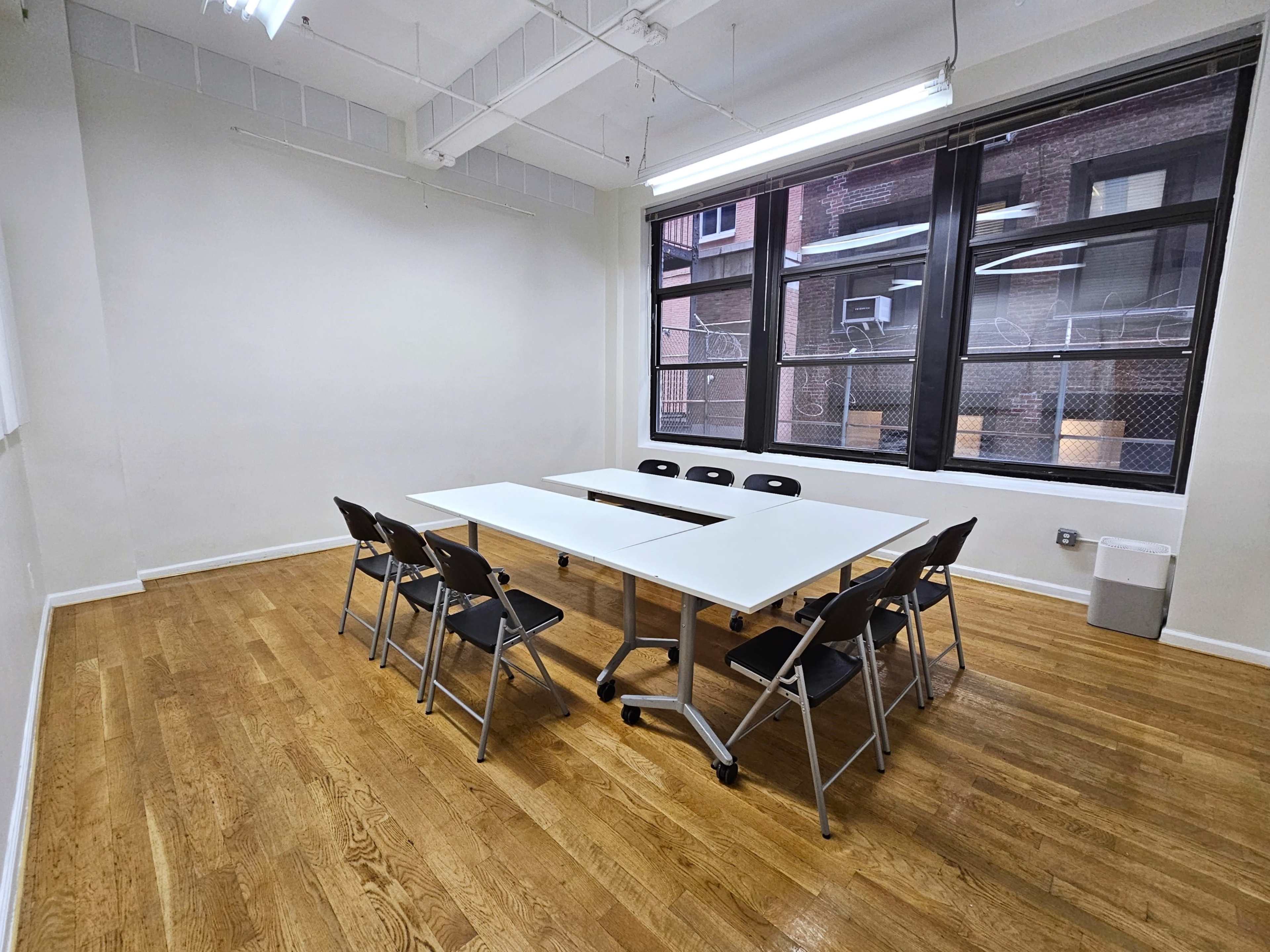 A conference room with a large table surrounded by black chairs and windows overlooking an urban exterior.