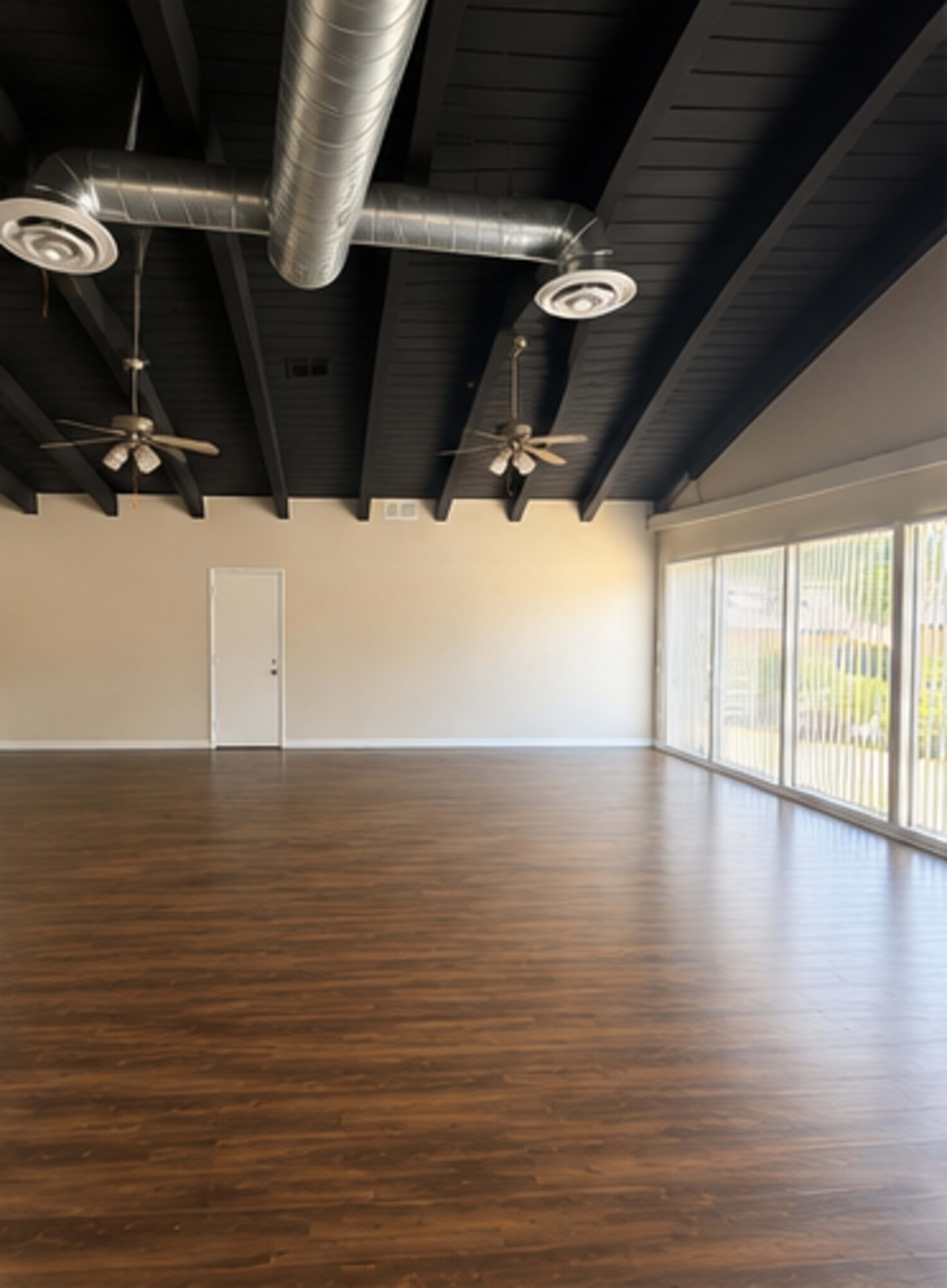 The image shows an empty room with hardwood floors, with large windows and two ceiling fans under a vaulted ceiling.