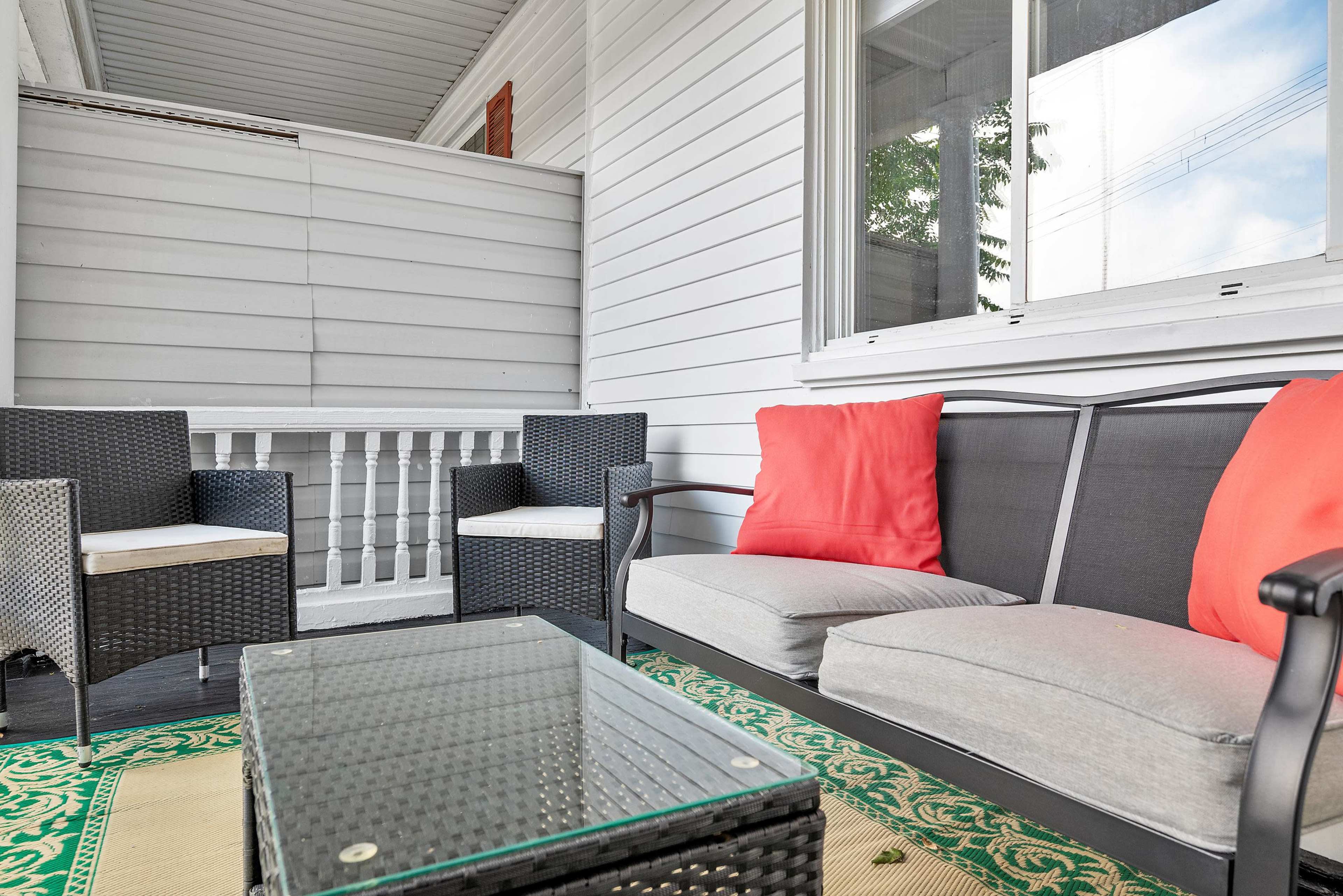 A small outdoor seating area with black wicker furniture, including two chairs and a couch, arranged around a glass-topped table on a patterned rug.