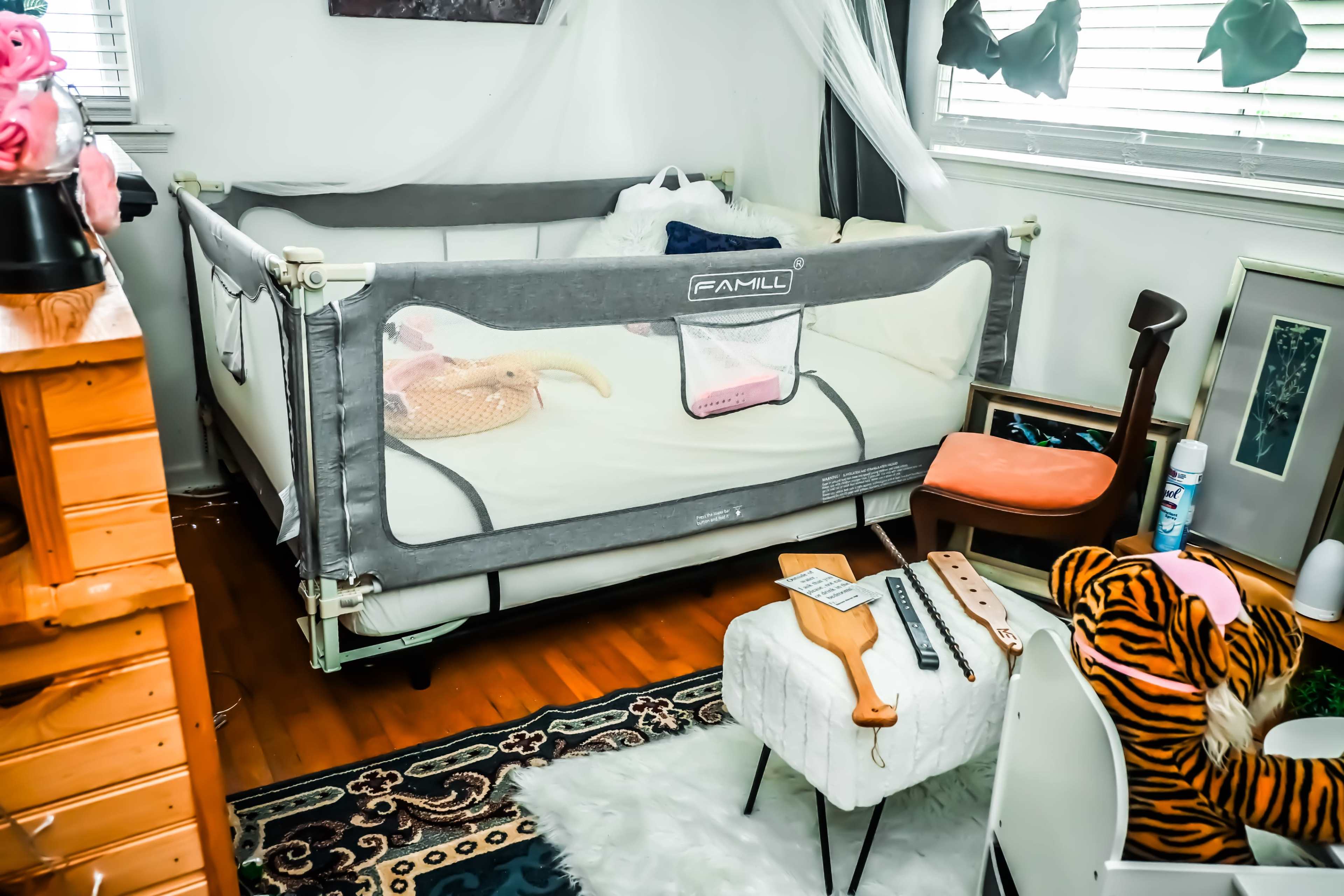 The image shows a room with a portable crib, a chair, a small table, and various decorative items scattered around.