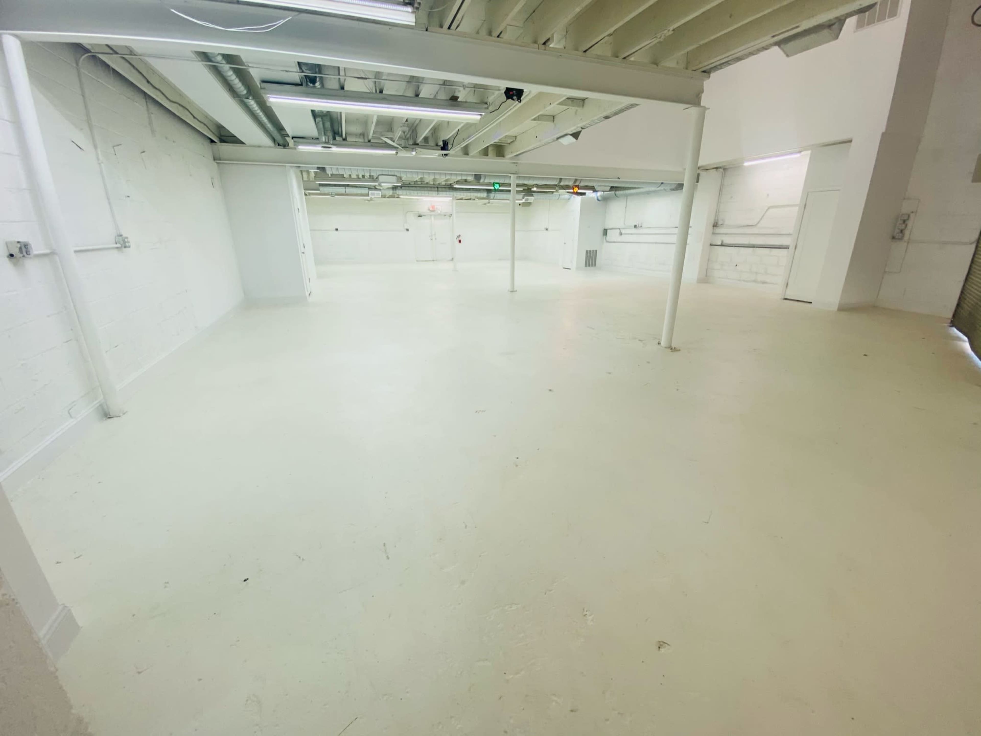 A spacious, empty warehouse interior with a white floor and exposed ceiling beams.