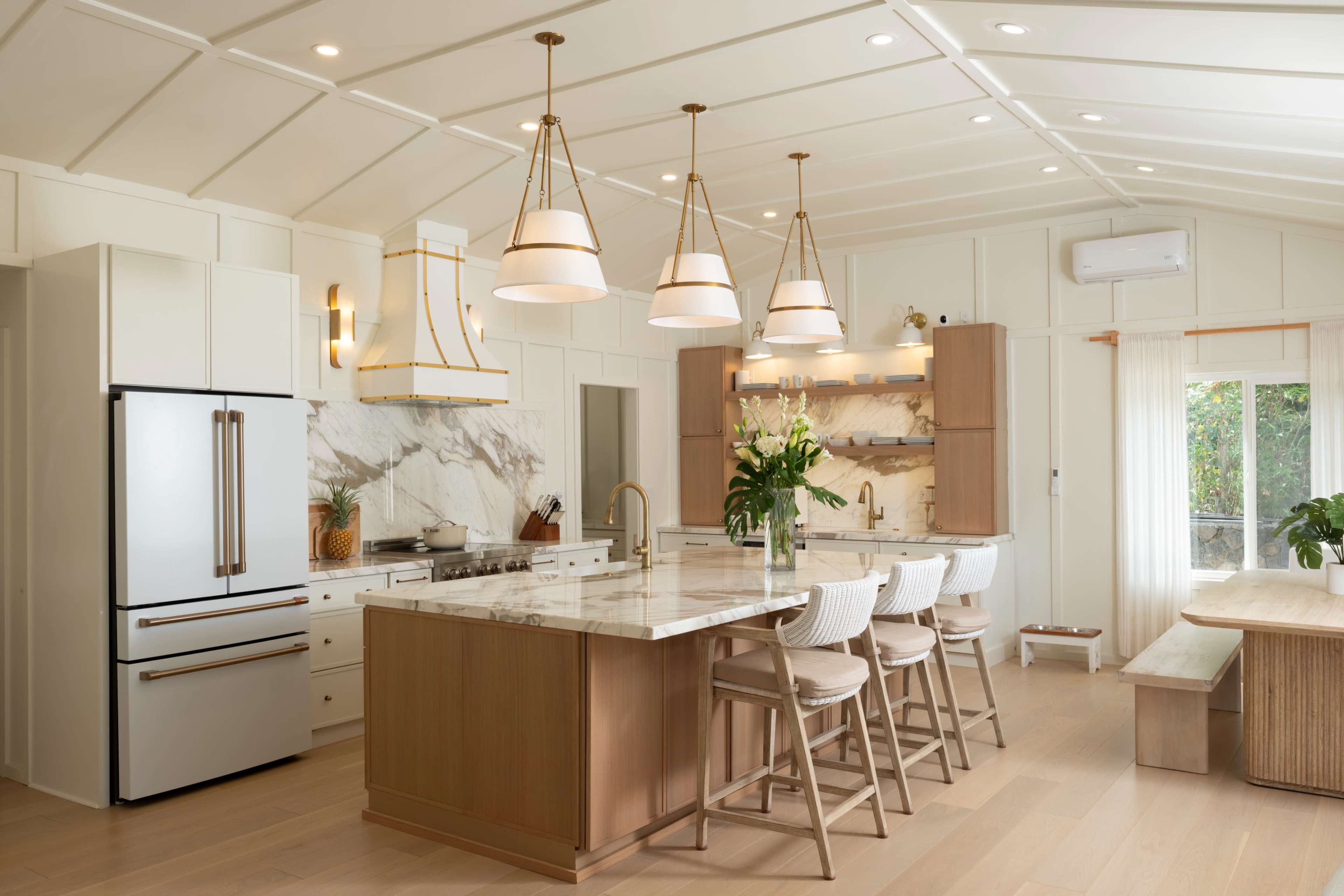 The image features a modern kitchen with a large marble island, pendant lights, and a mix of wooden and white cabinetry.