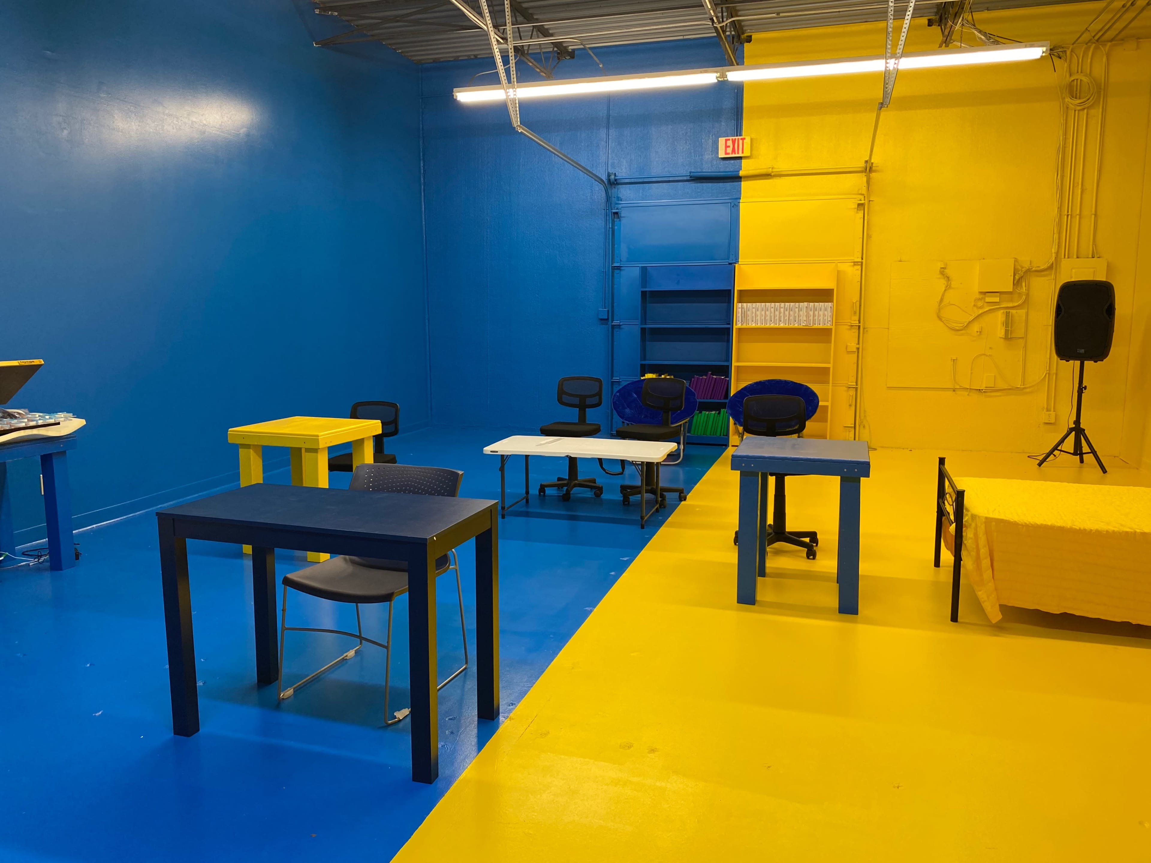 The room features blue and yellow walls with several desks and chairs arranged on a brightly painted floor.