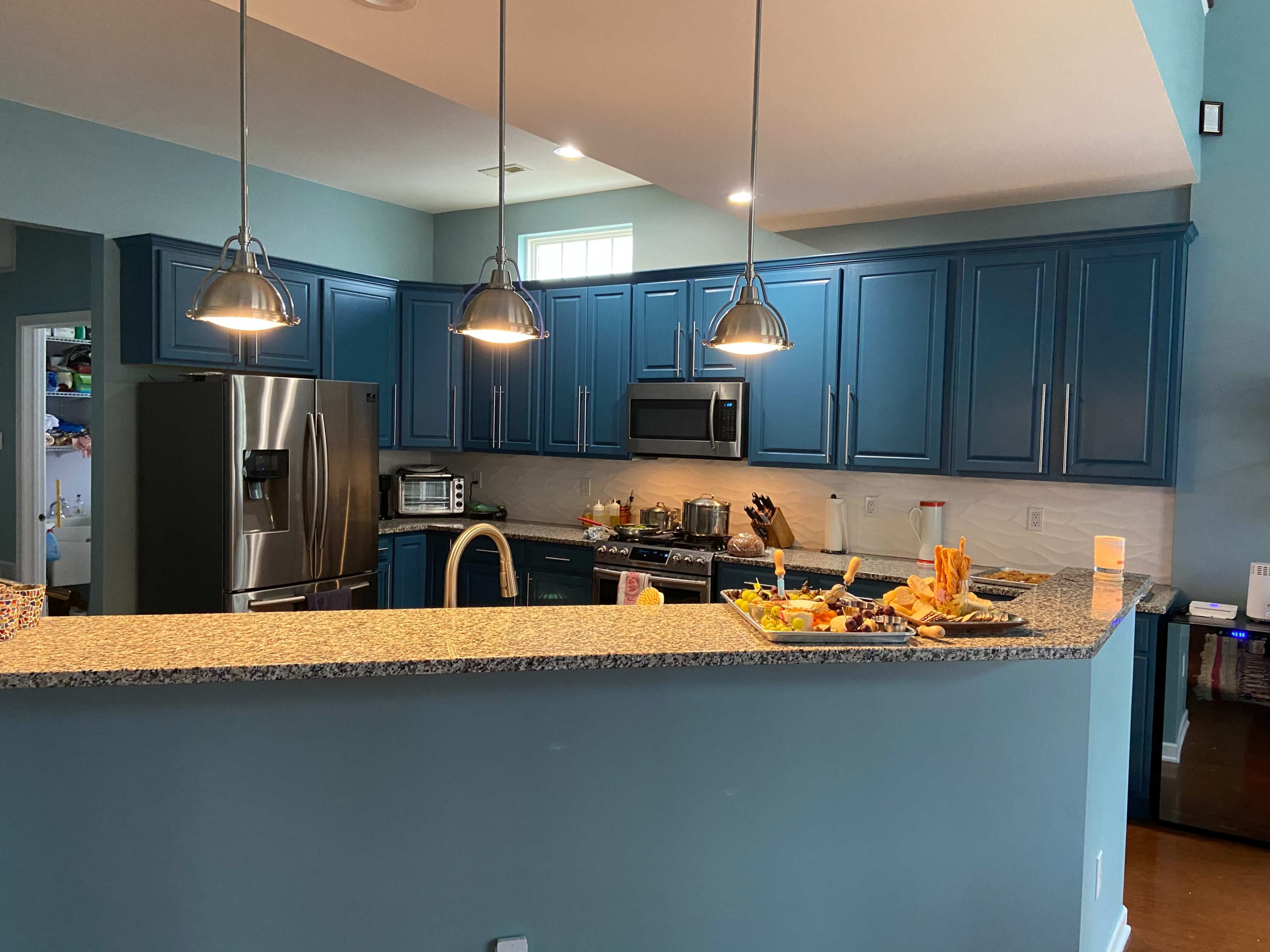 A modern kitchen with blue cabinetry, granite countertops, and pendant lighting, featuring a variety of food items on the island.