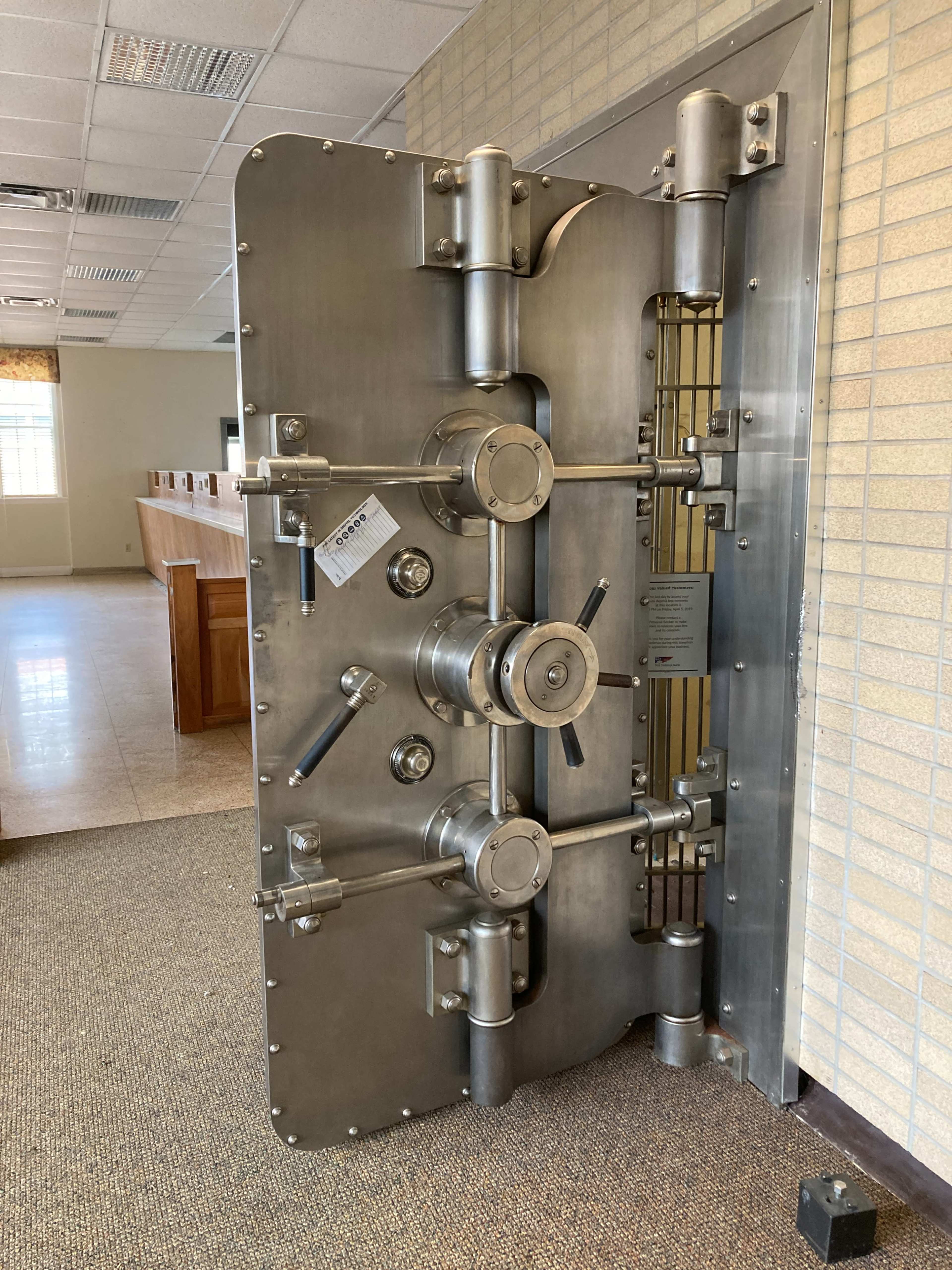 A large, metal bank vault door is partially open, revealing a secure interior space.