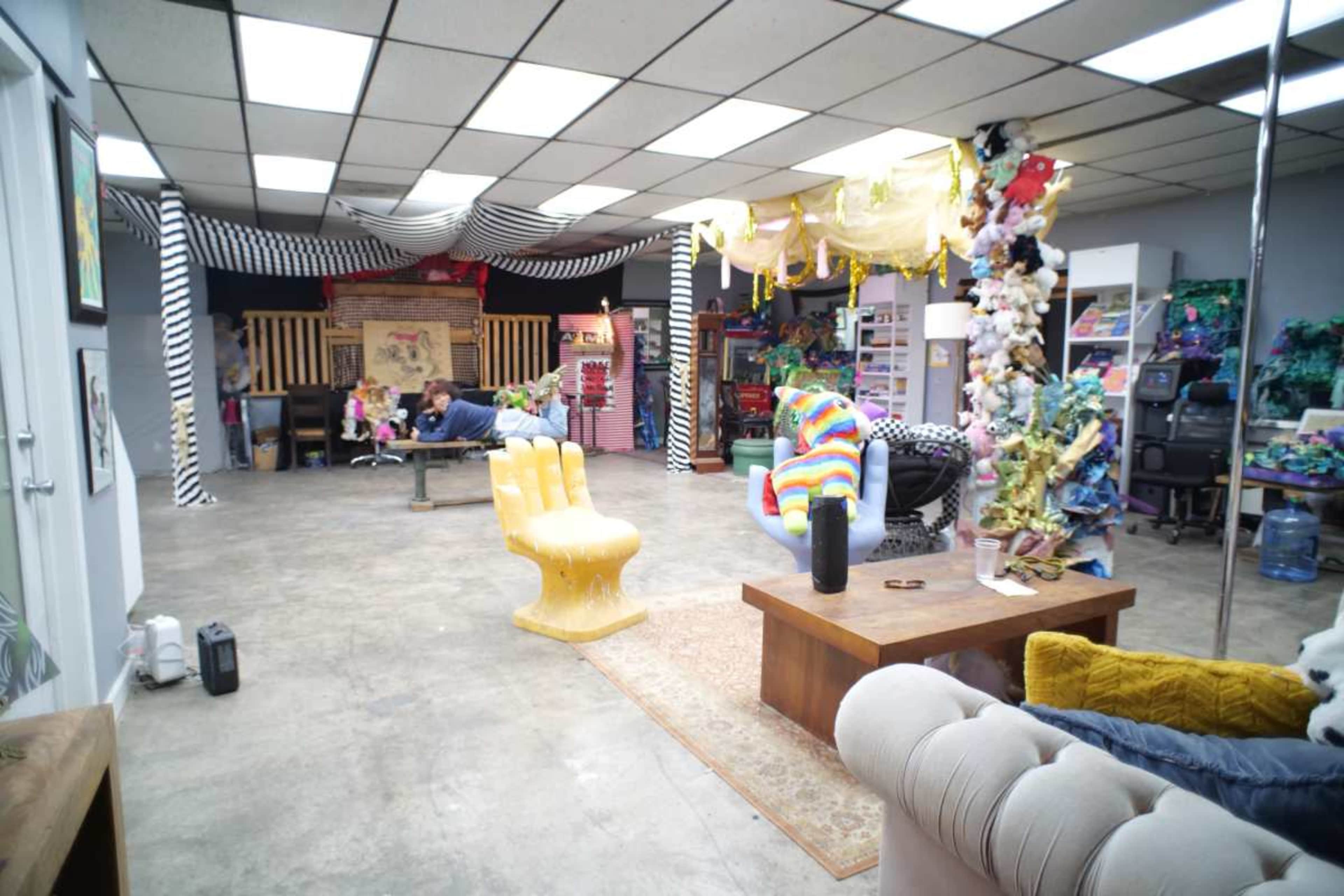 The image shows a spacious creative studio filled with colorful decorations, various art supplies, and distinct furniture pieces.