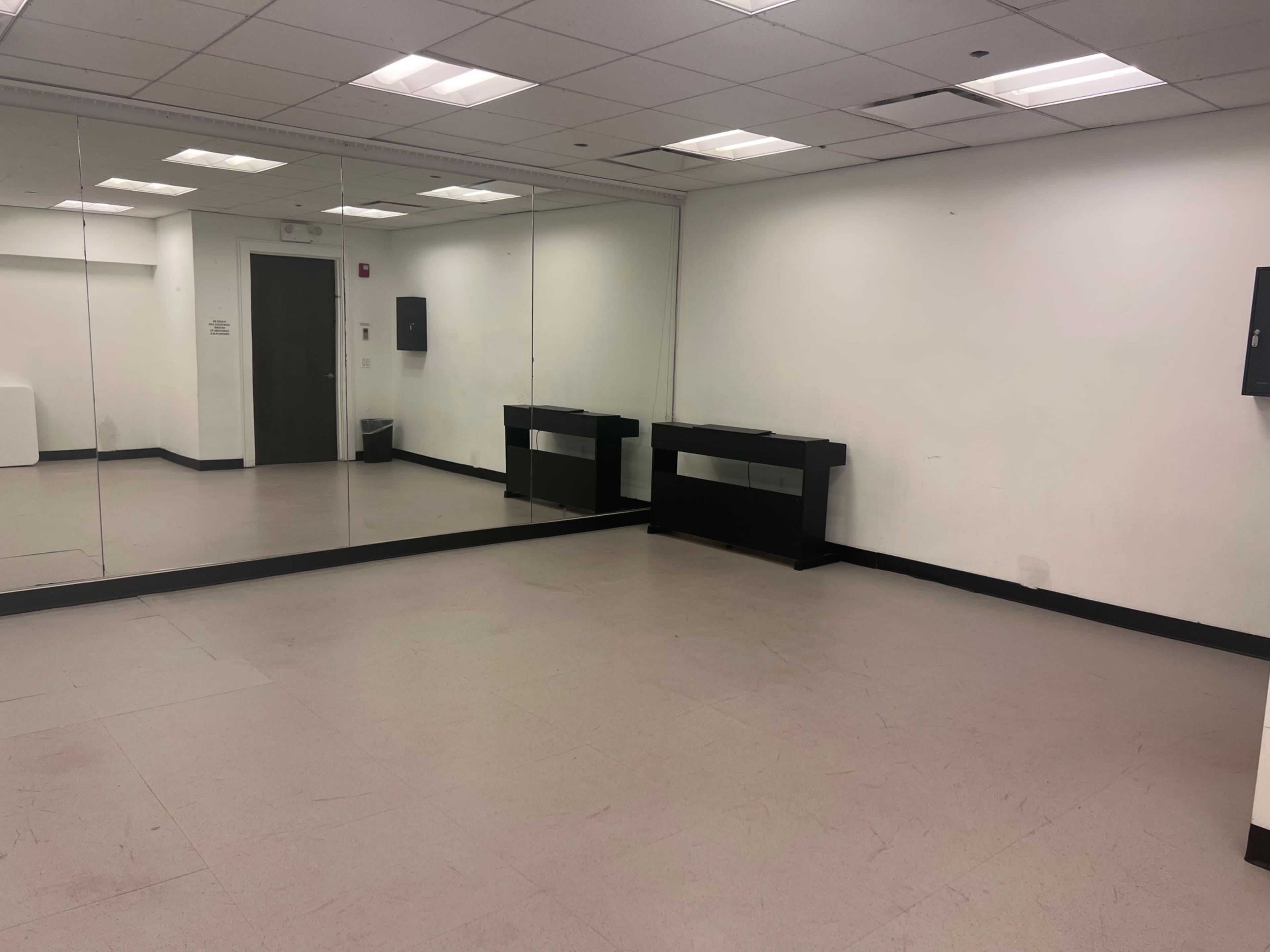 The image shows a spacious room with mirrors on one wall, a black console table, and plain white walls.