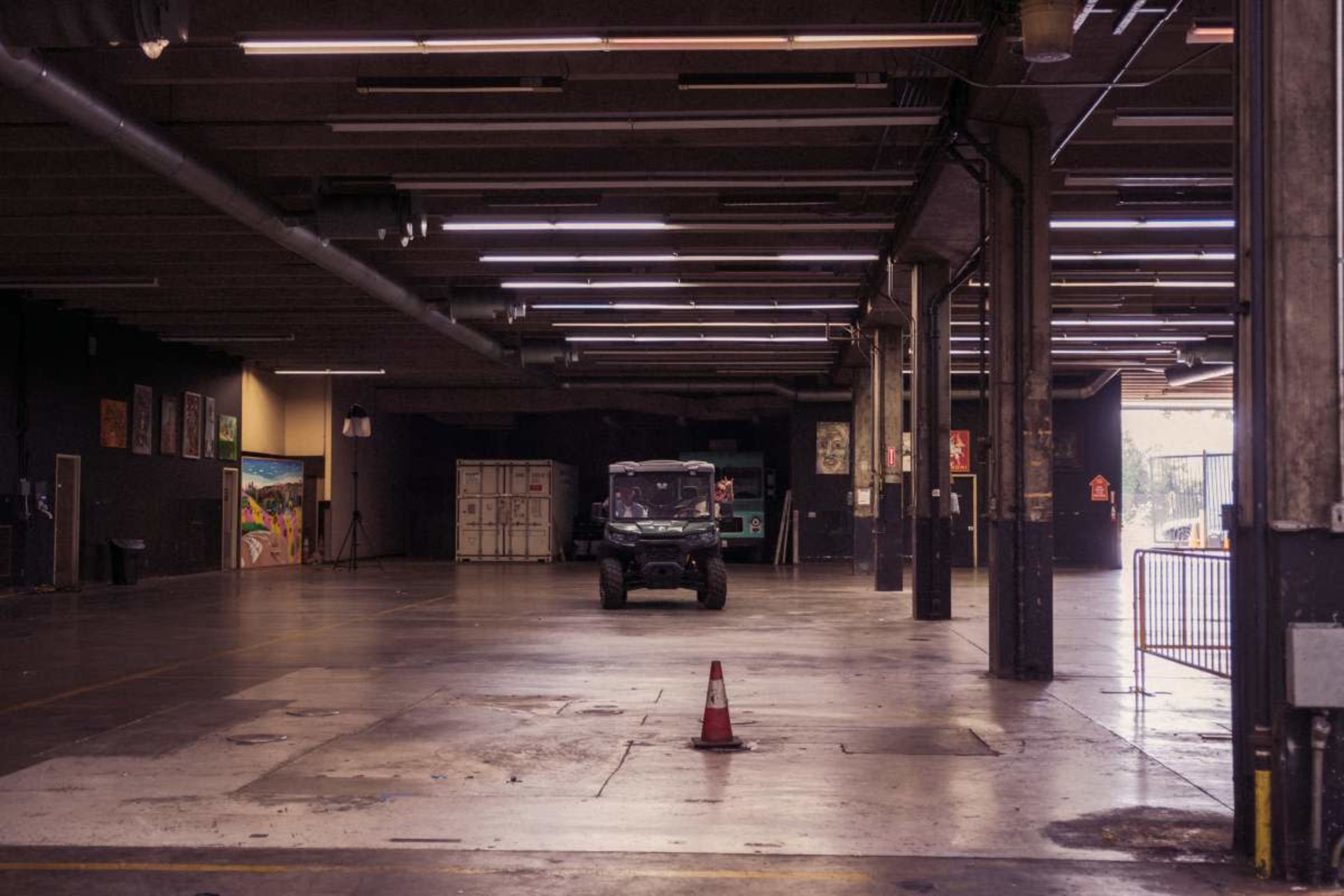 A green vehicle is parked in a large, empty warehouse space with exposed beams and minimal lighting.