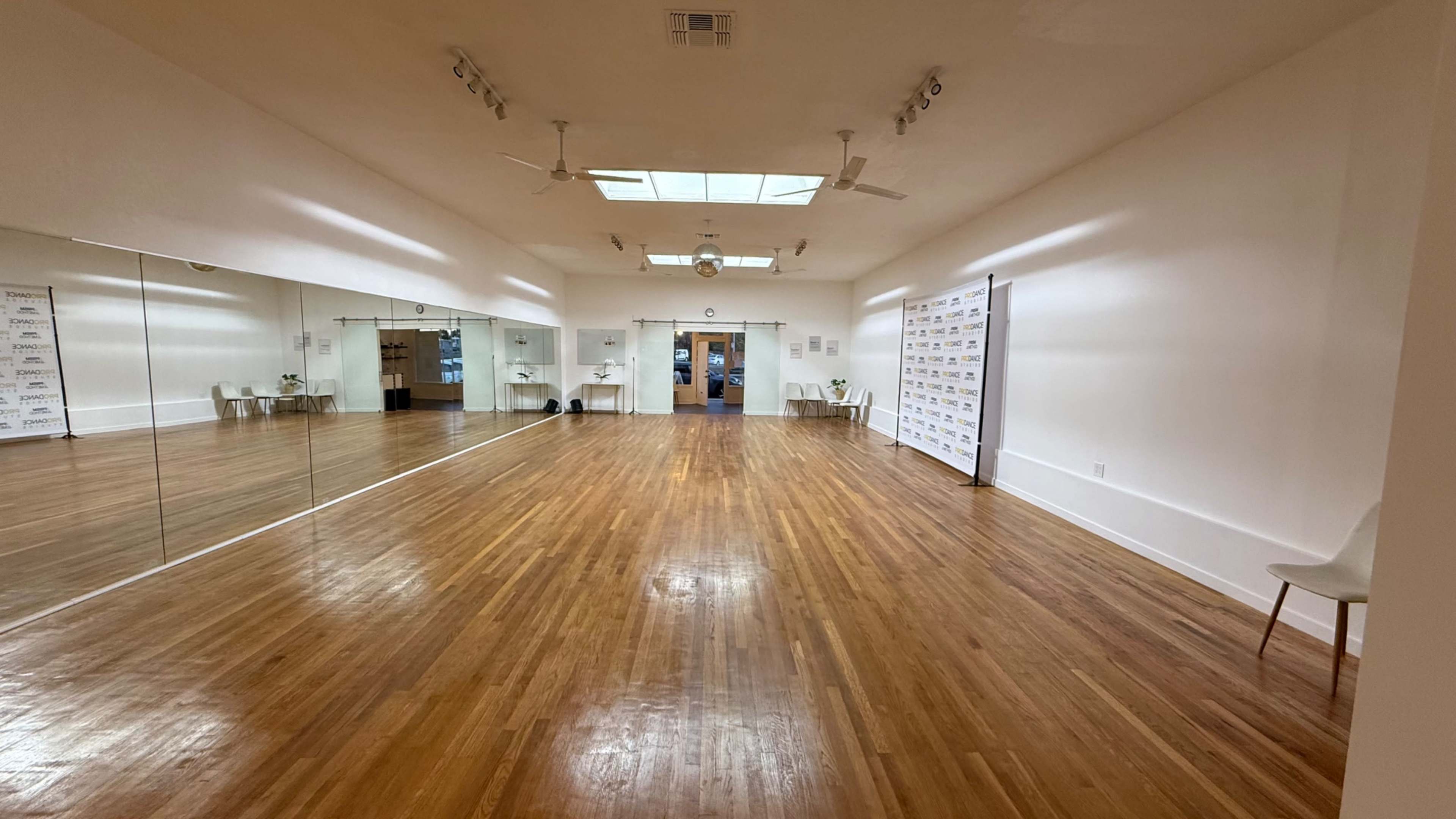 The image shows a spacious, empty dance studio with polished wooden floors, large mirrors on one wall, and minimal decoration.