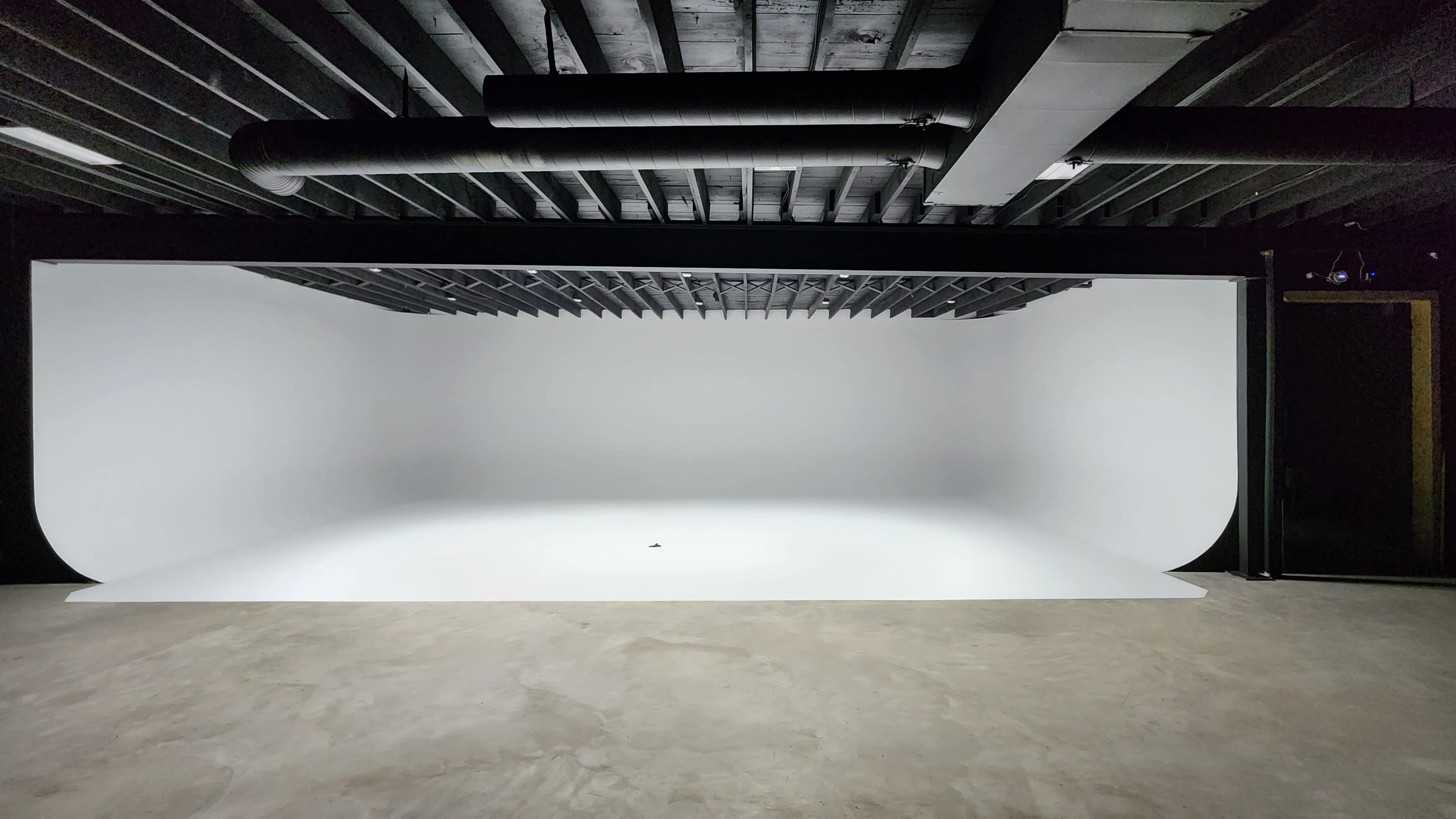 The image shows a spacious studio with a seamless white backdrop and concrete flooring.
