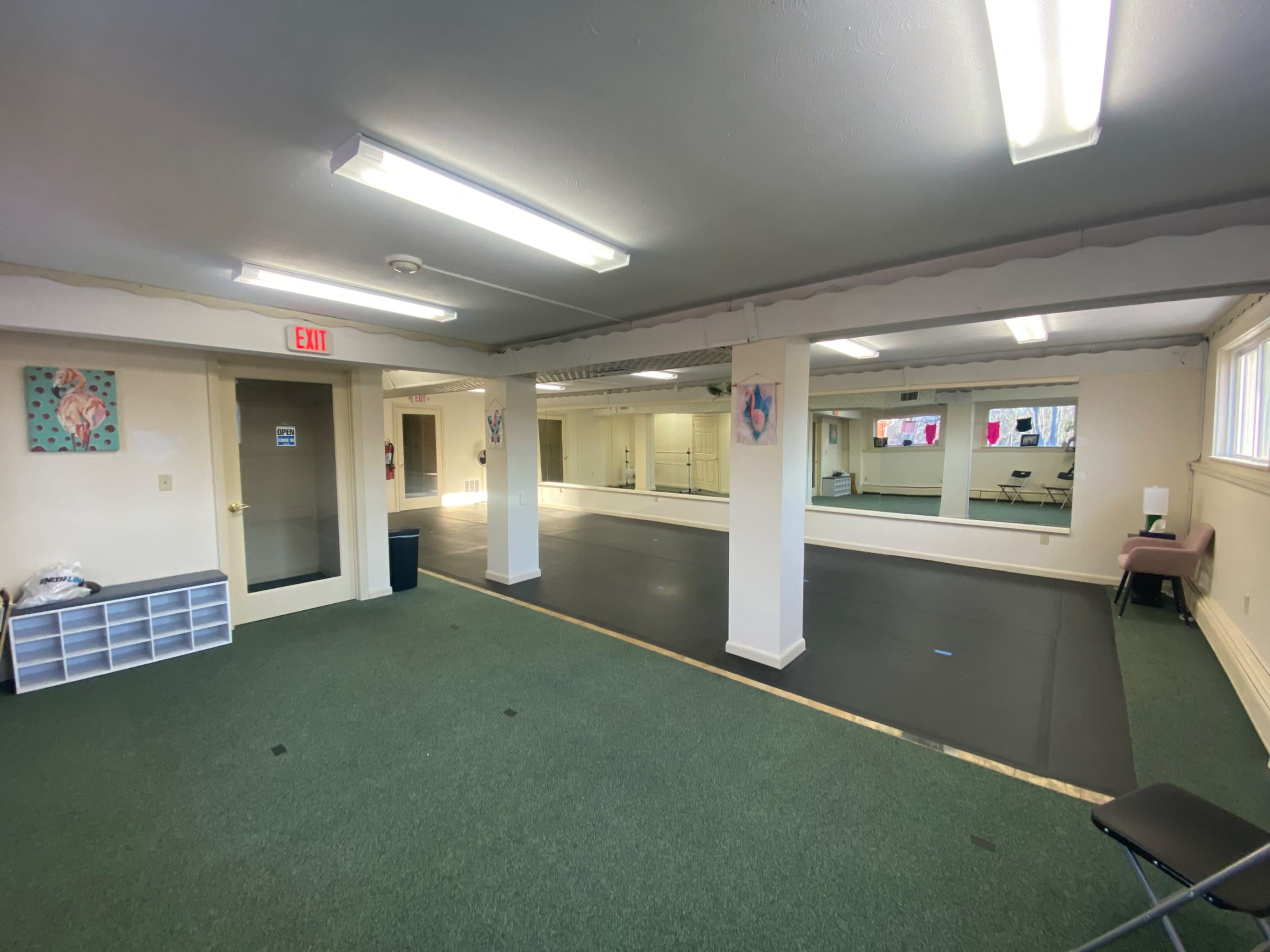 A spacious room with green carpet, fluorescent lighting, and mirrored walls, used for activities such as dance or fitness.