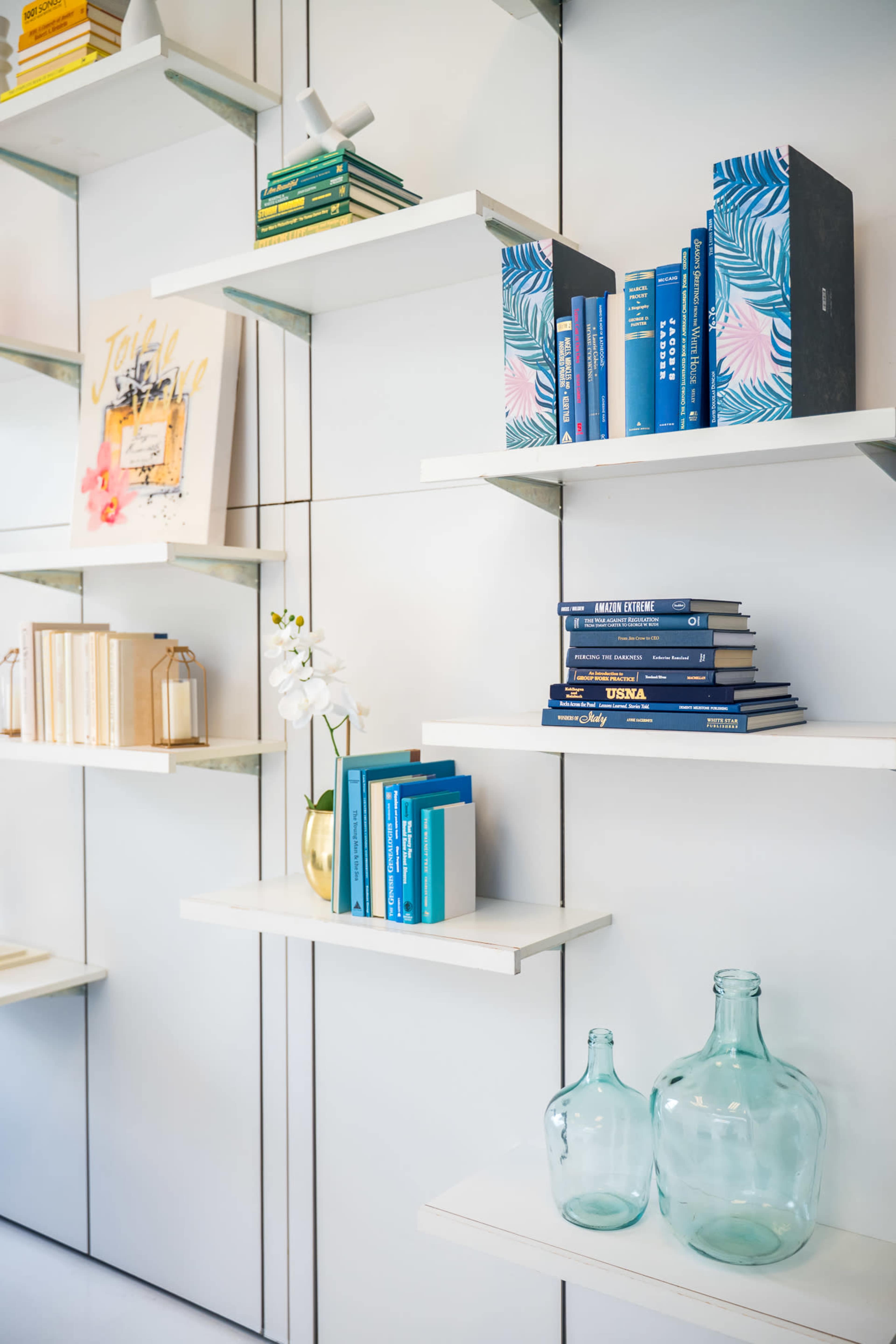 The image shows a modern bookshelf with various books and decorative items arranged on white shelves.