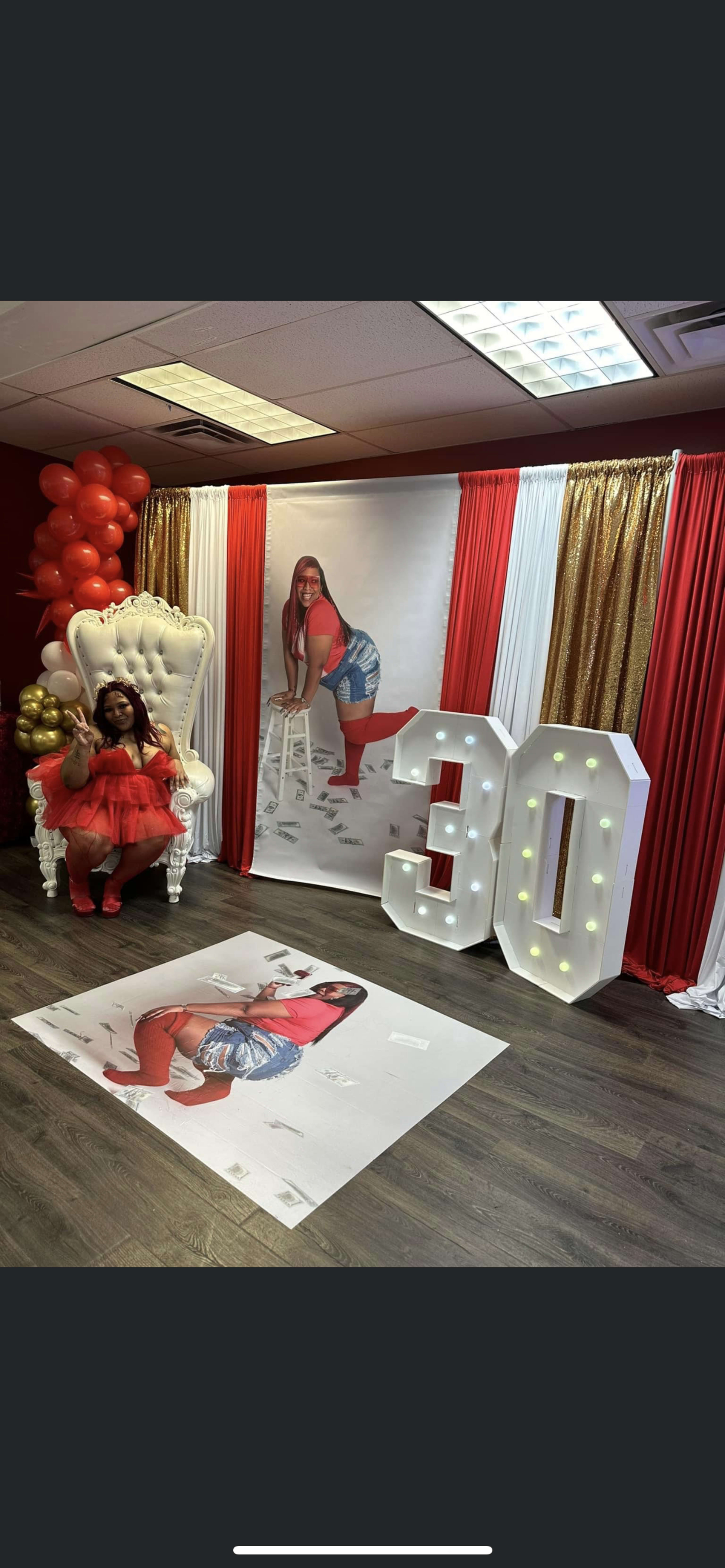 A woman in a red outfit sits on an ornate white chair in a decorated room featuring a large "30" display and festive balloons.