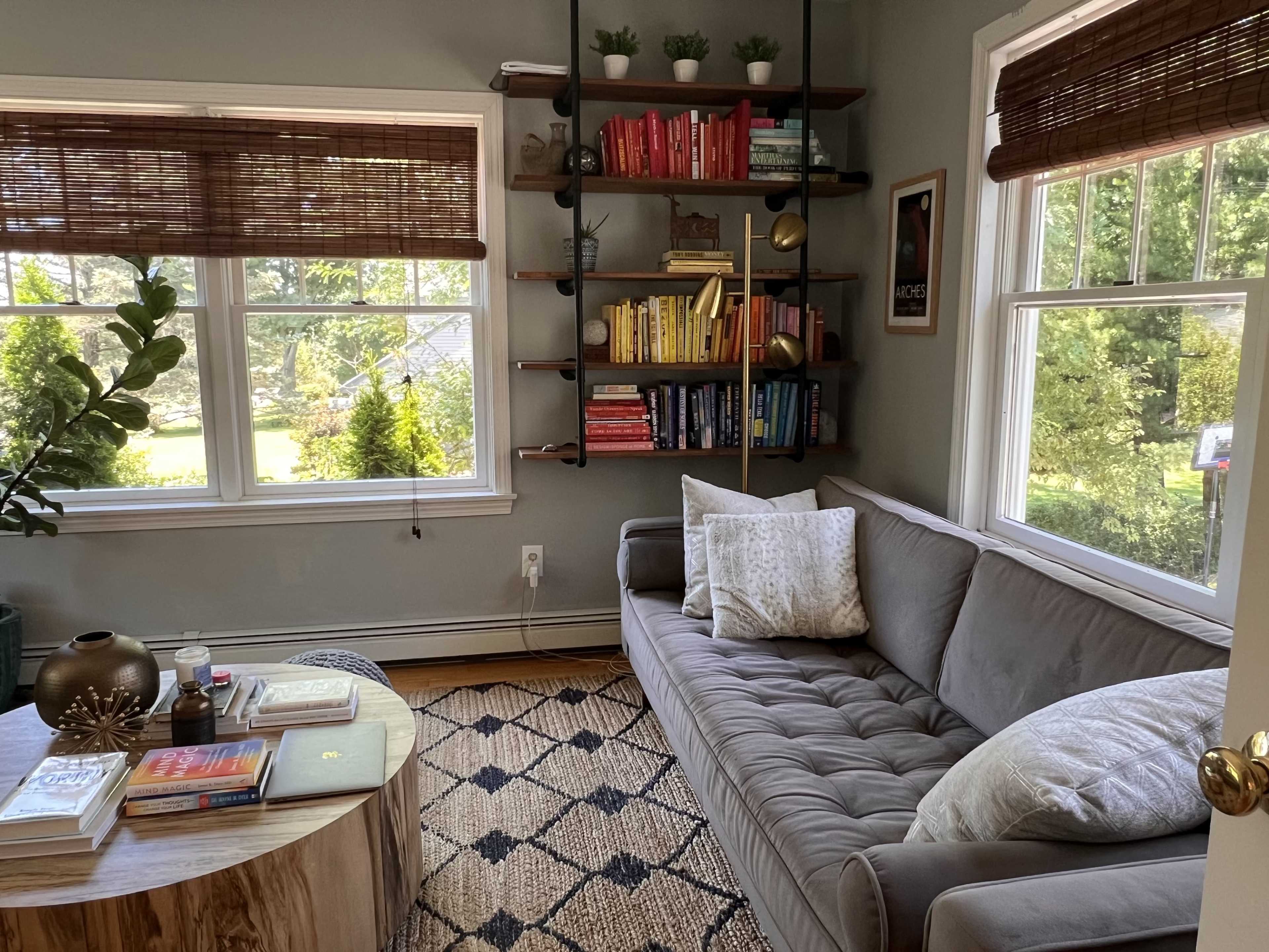A cozy living room with a gray couch, a round wooden coffee table, and bookshelves filled with colorful books against a light gray wall.