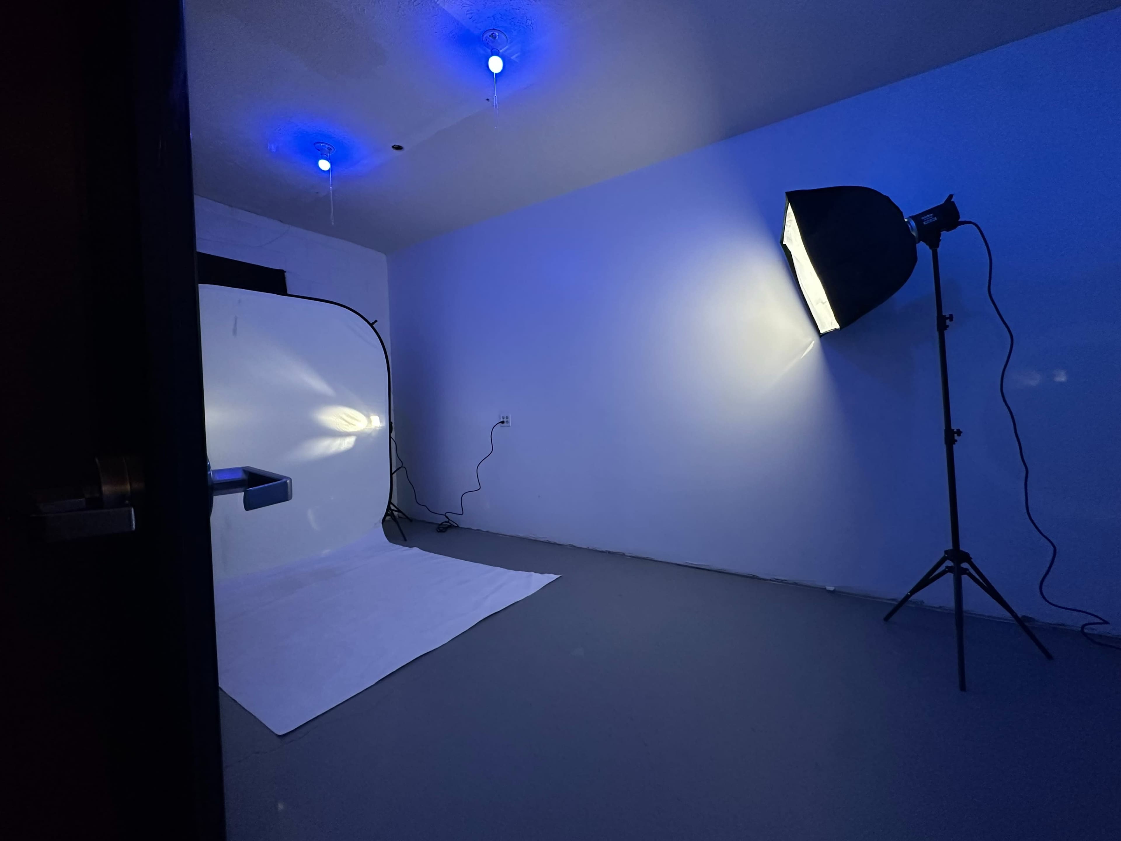 A photography studio with a white backdrop, a lighting setup, and blue lighting fixtures on the ceiling.
