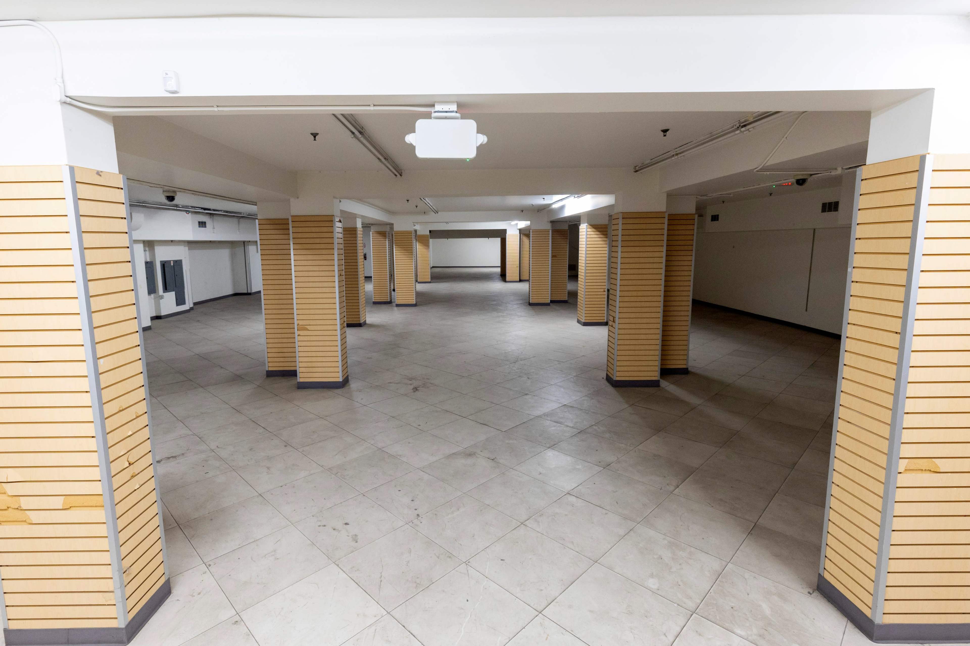 The image shows an empty, open space with tiled floors and wooden paneling on the walls, supported by several columns.