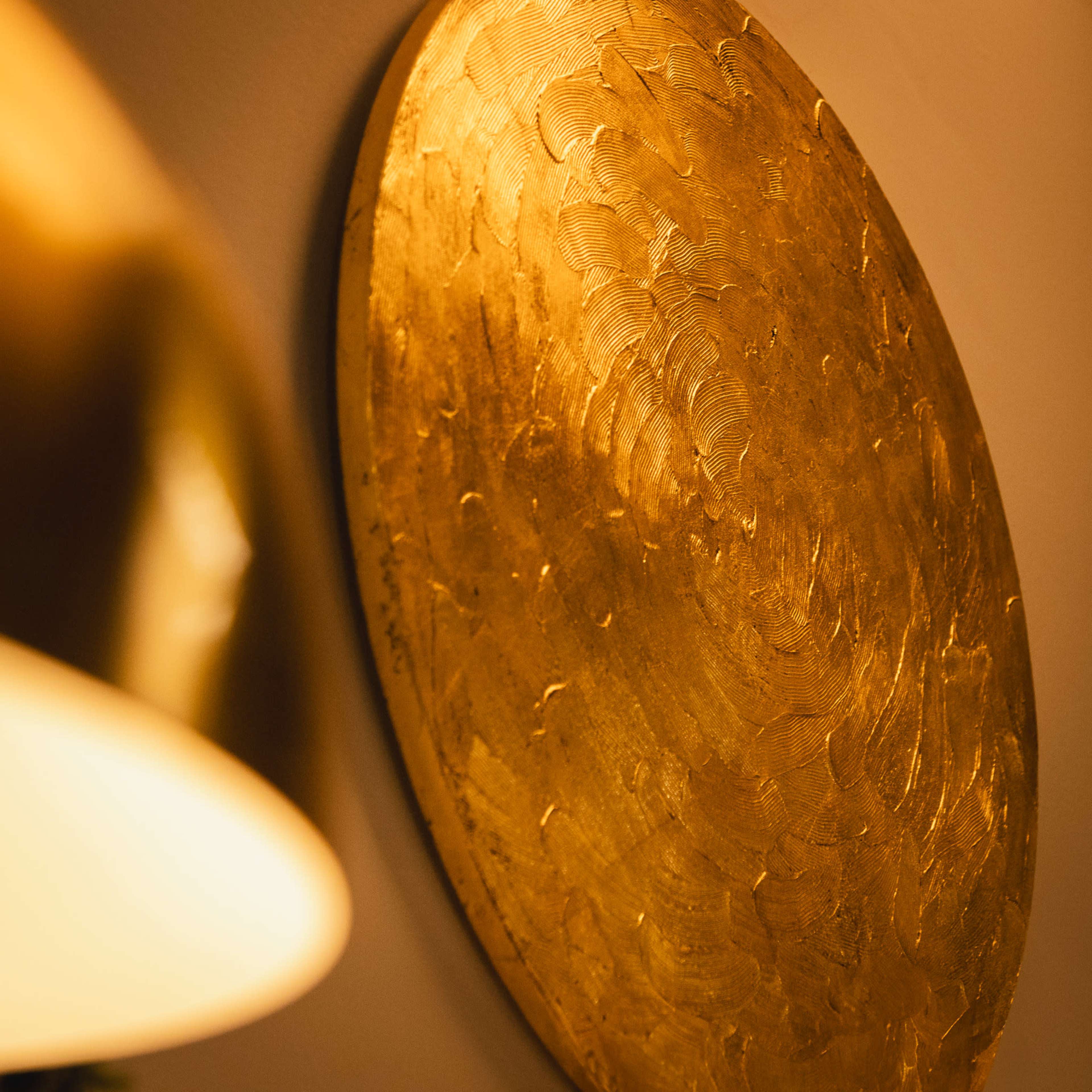 The image features a round, textured gold wall decoration illuminated by warm light.