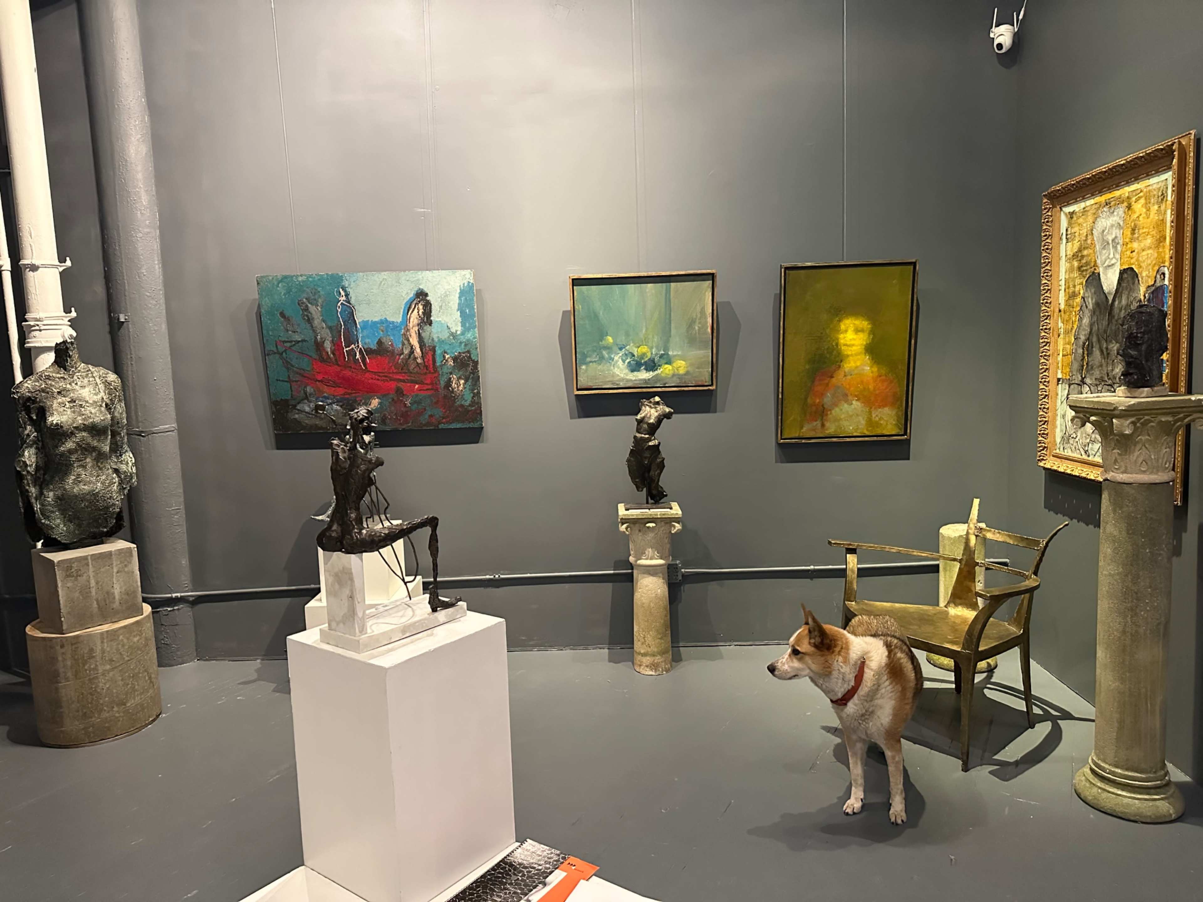 The scene shows an art gallery featuring various paintings and sculptures, with a dog standing on the floor among the exhibits.
