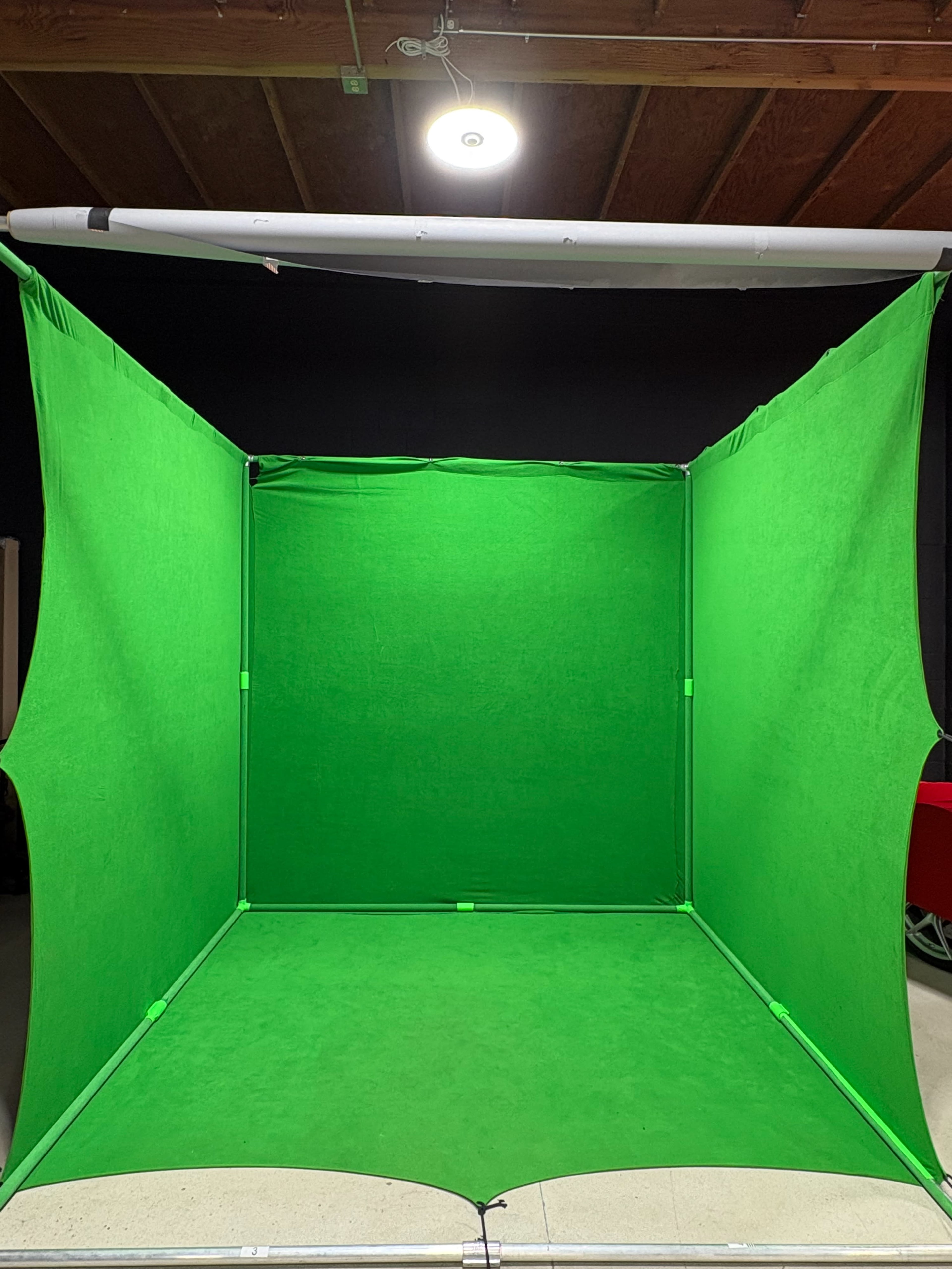 The image shows a green screen studio setup with large green fabric panels forming a box-like structure.