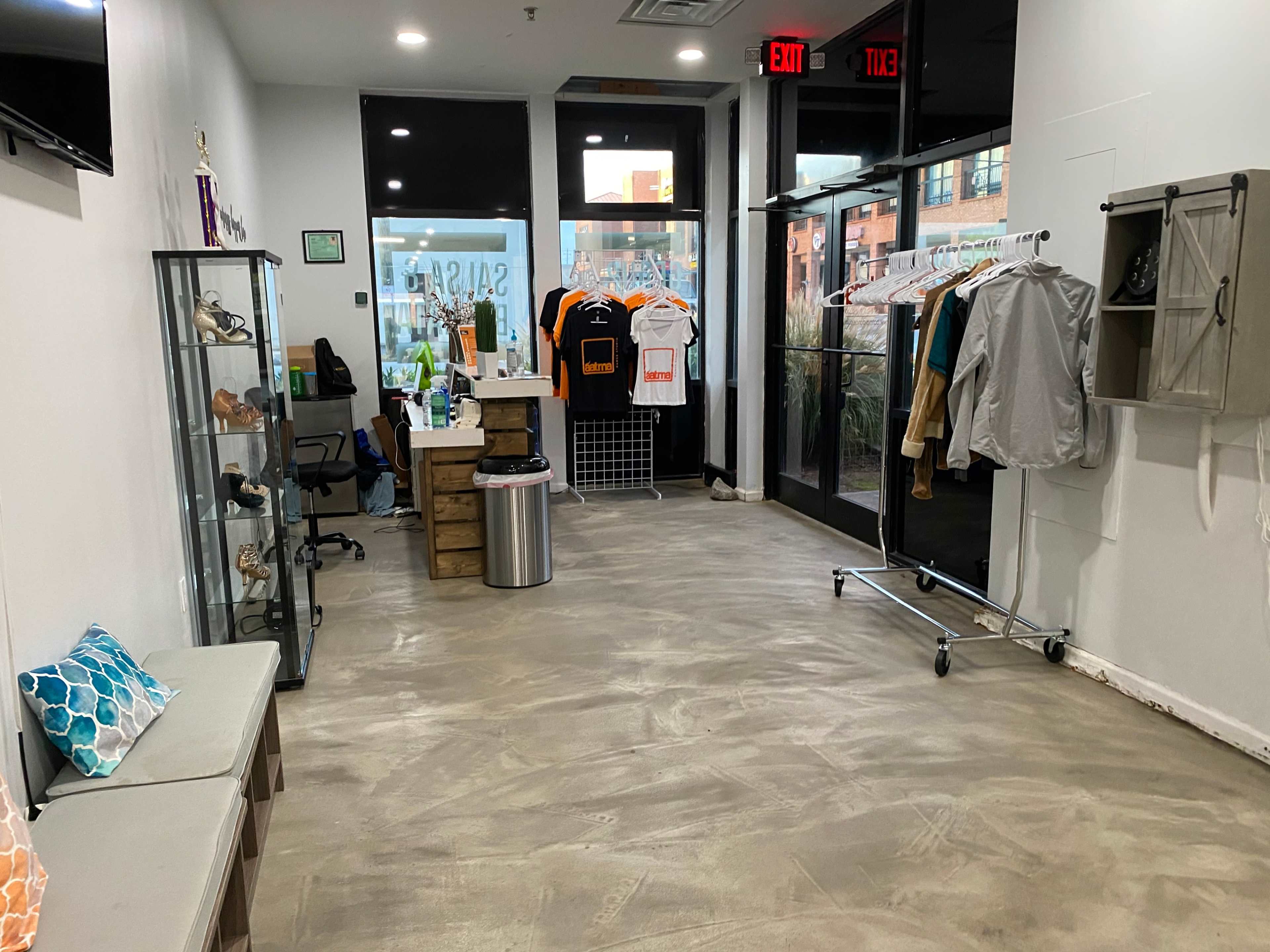 An empty retail space with a gray concrete floor, display cases, clothing racks, and a checkout counter near large glass doors.