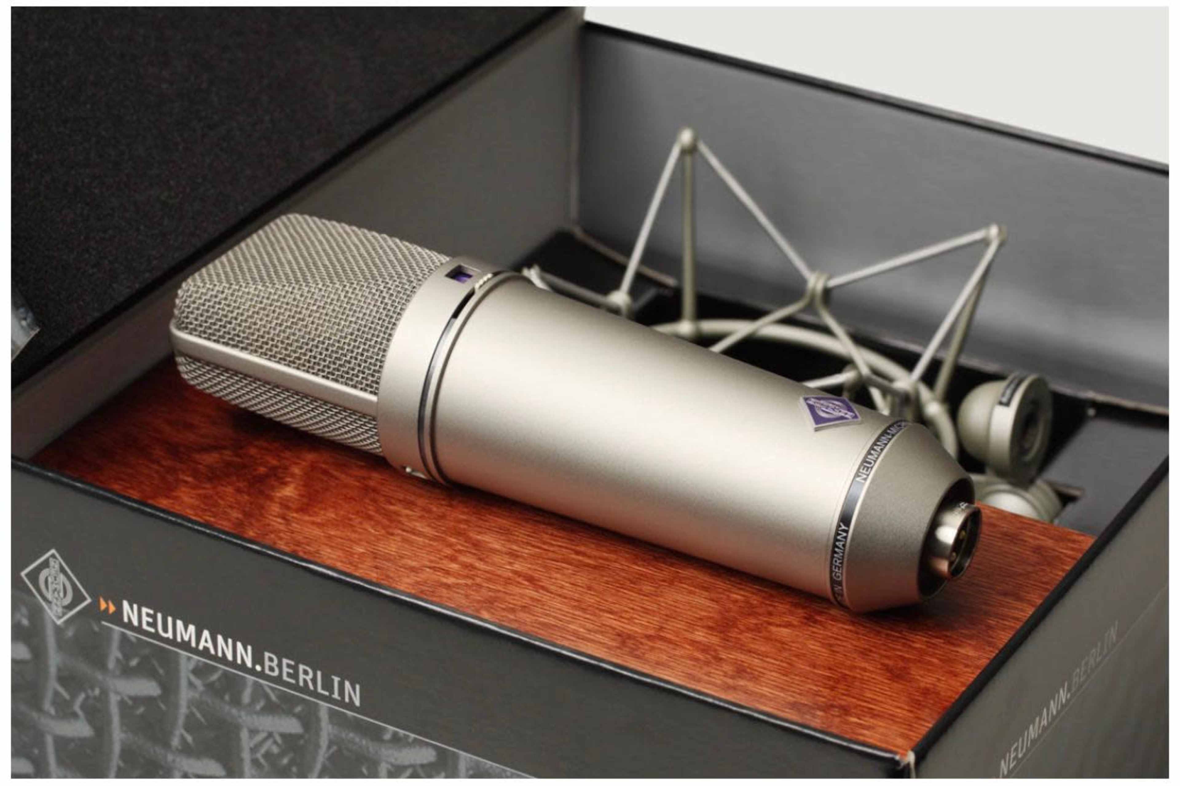 A silver condenser microphone is placed inside a black box alongside its shock mount and foam padding.