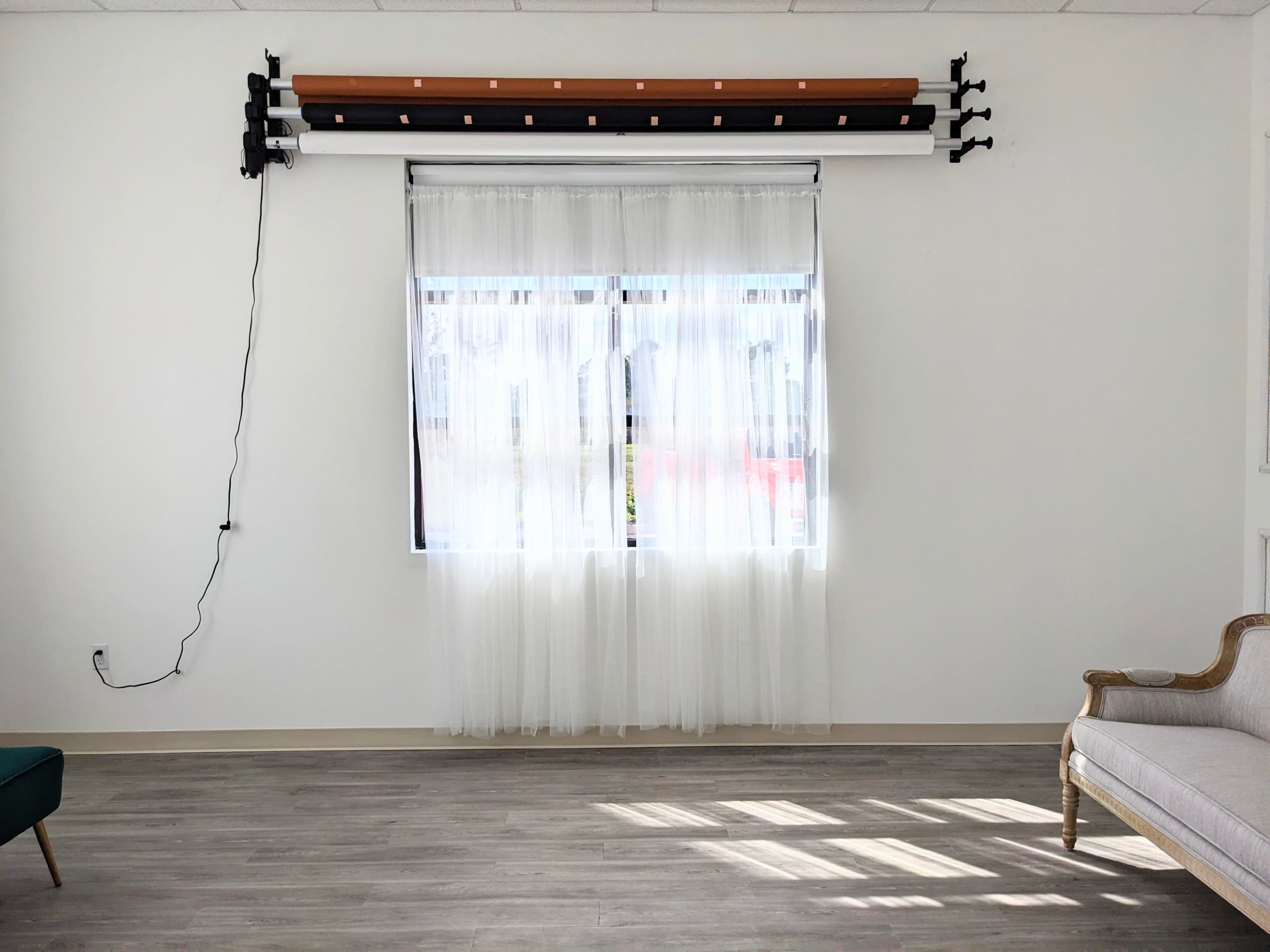 A bright, minimalist room with a large window covered by sheer curtains, a light wooden floor, and a single upholstered chair.