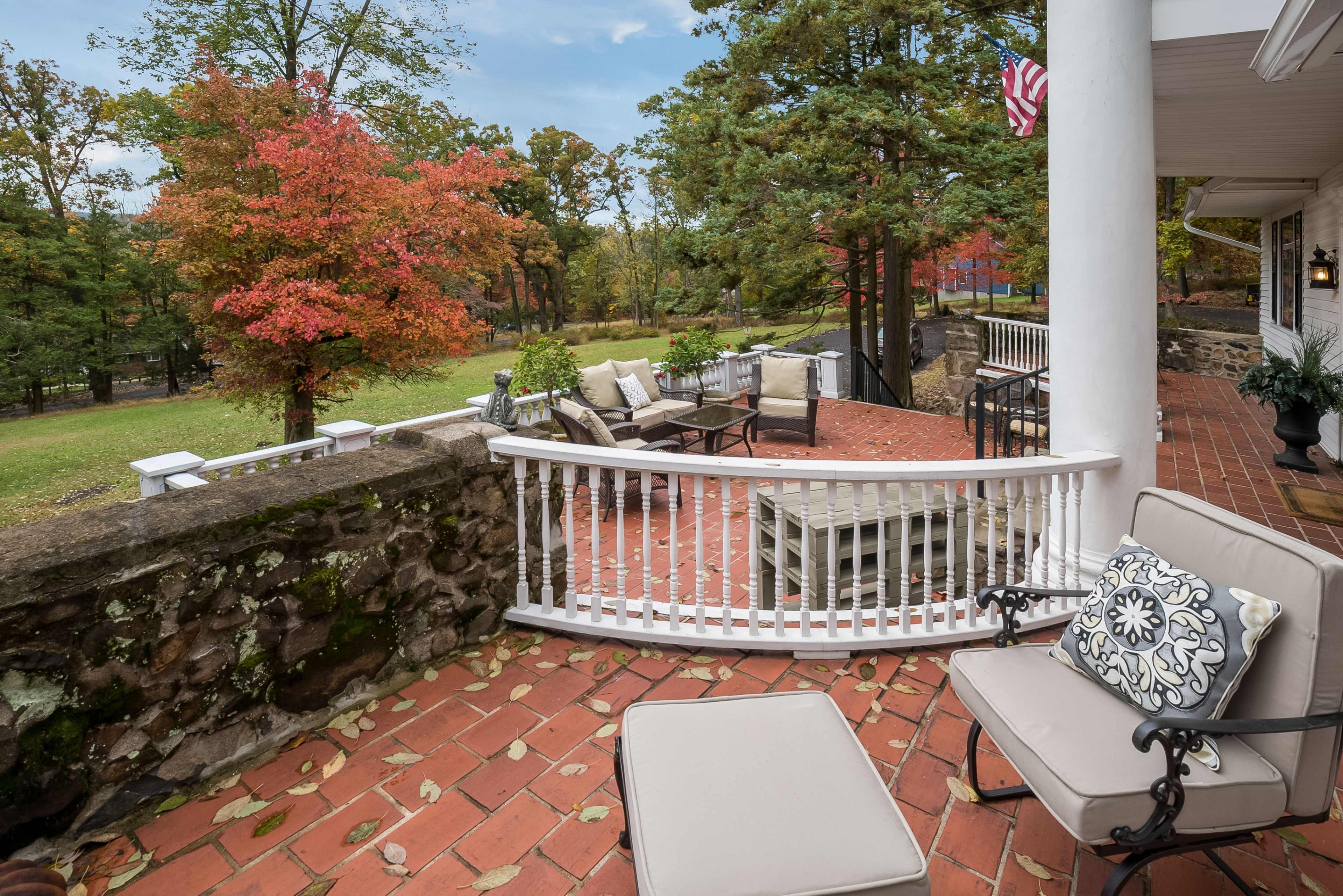 A brick patio area with outdoor furniture, surrounded by trees displaying autumn foliage.