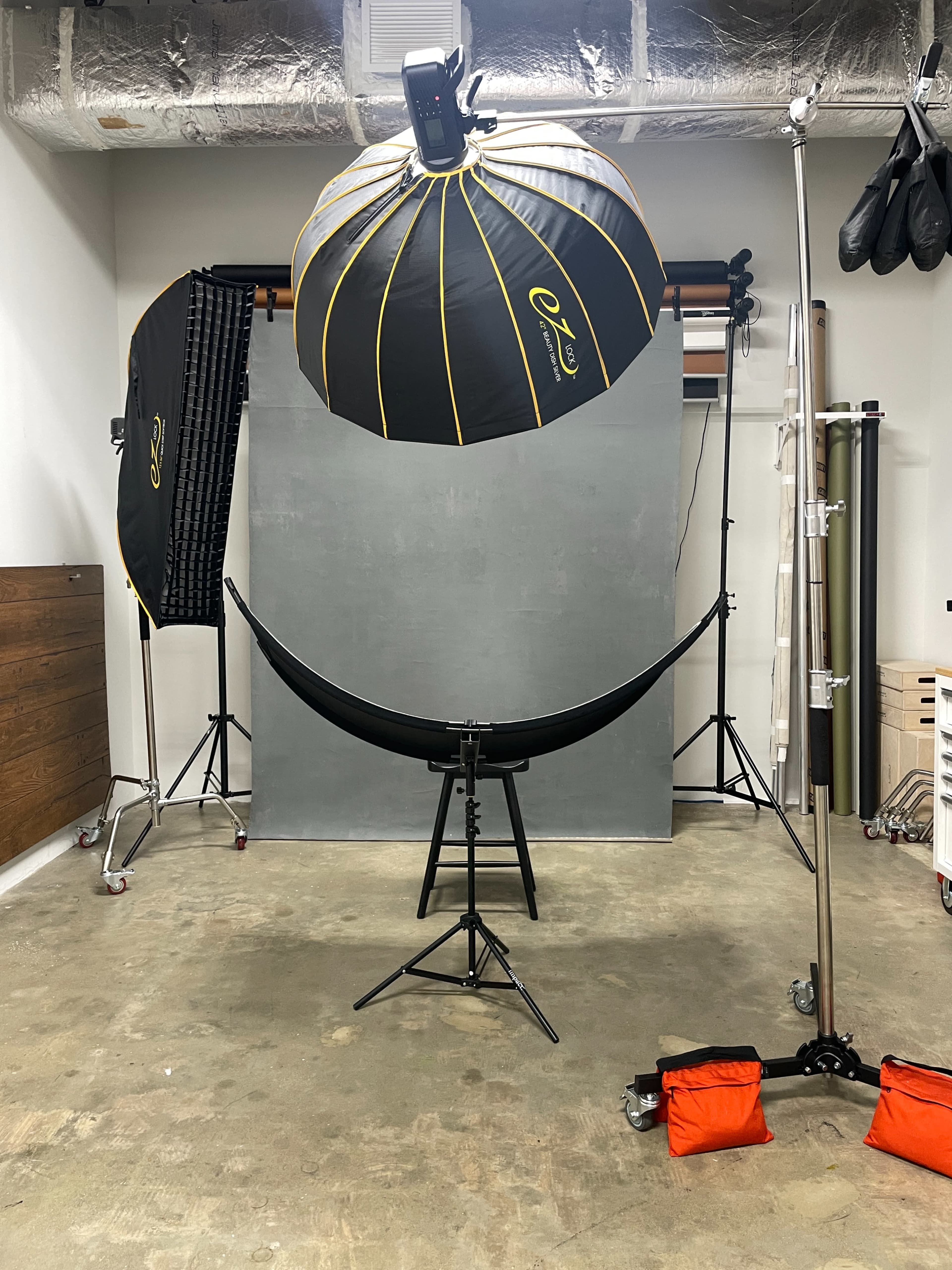 A photography studio setup featuring a gray backdrop, softbox lighting, and a curved black reflector positioned on a stand.