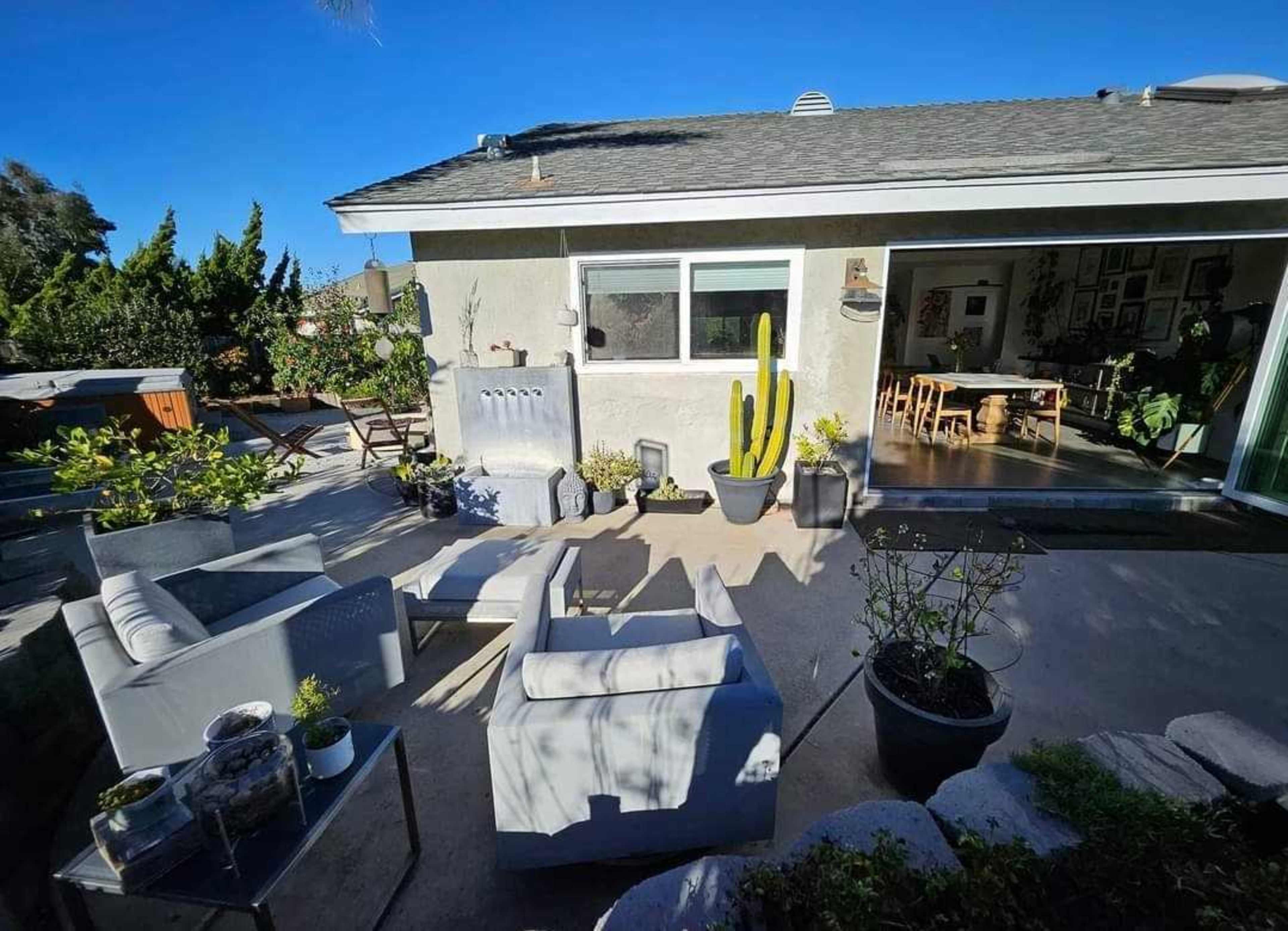 A patio area with gray furniture, a tall cactus, and a view of a house with a dining area visible through large glass doors.
