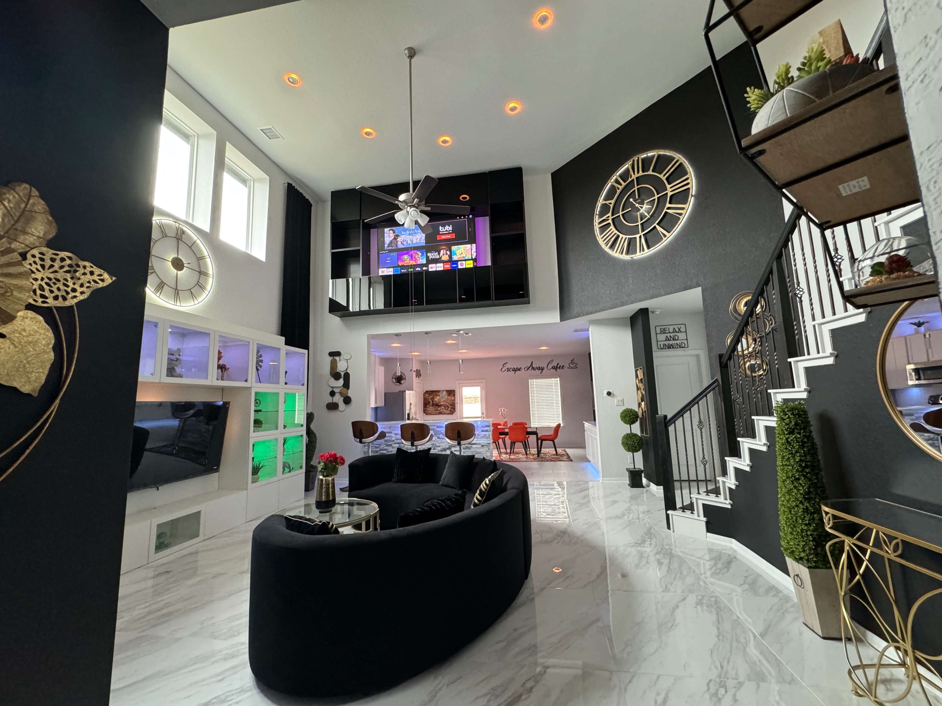 A modern living room features a circular sectional sofa, a wall-mounted television, and decorative gold accents against black and white walls.